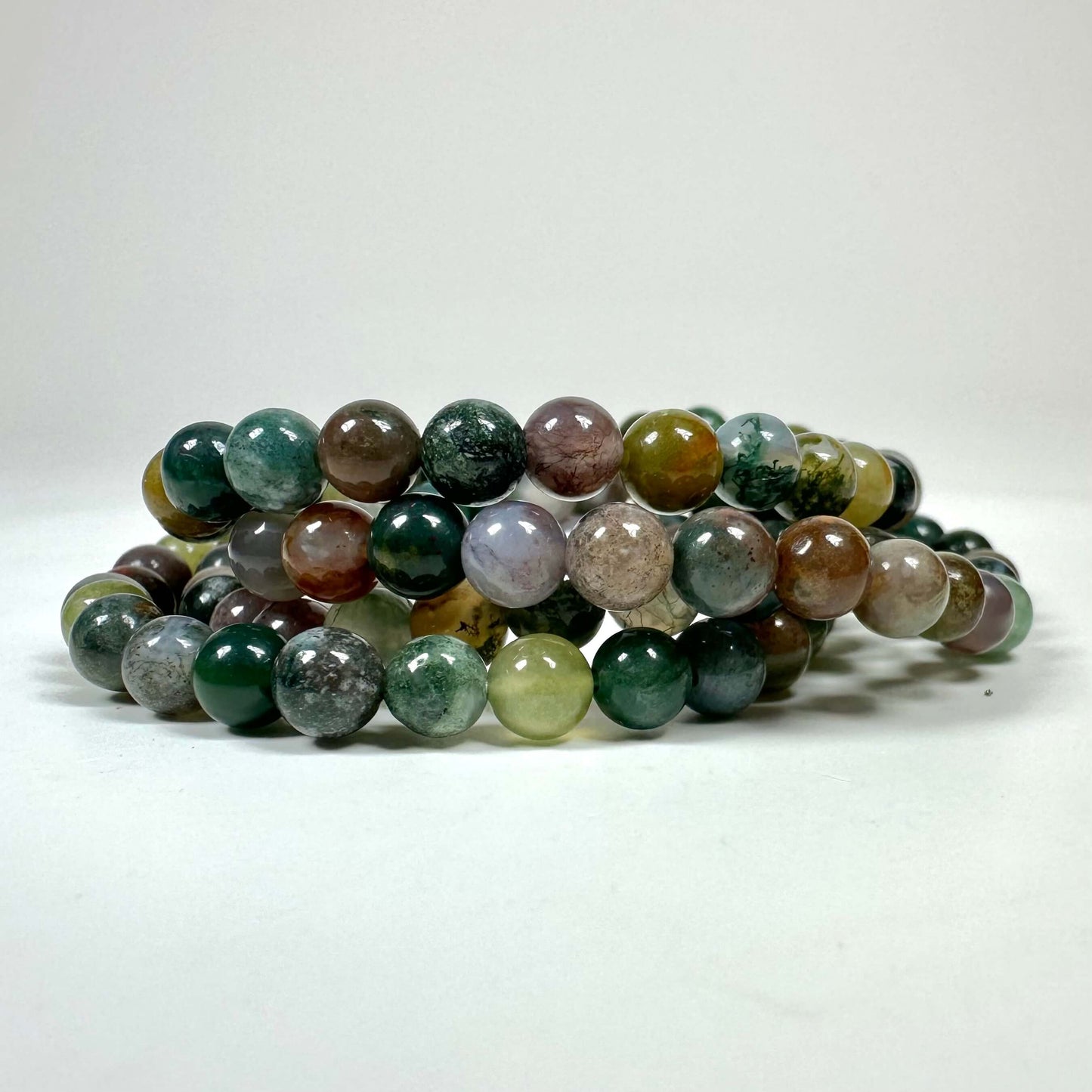 Armbånd med flerfarvede perler i grønne, brune og grå nuancer på en hvid baggrund.