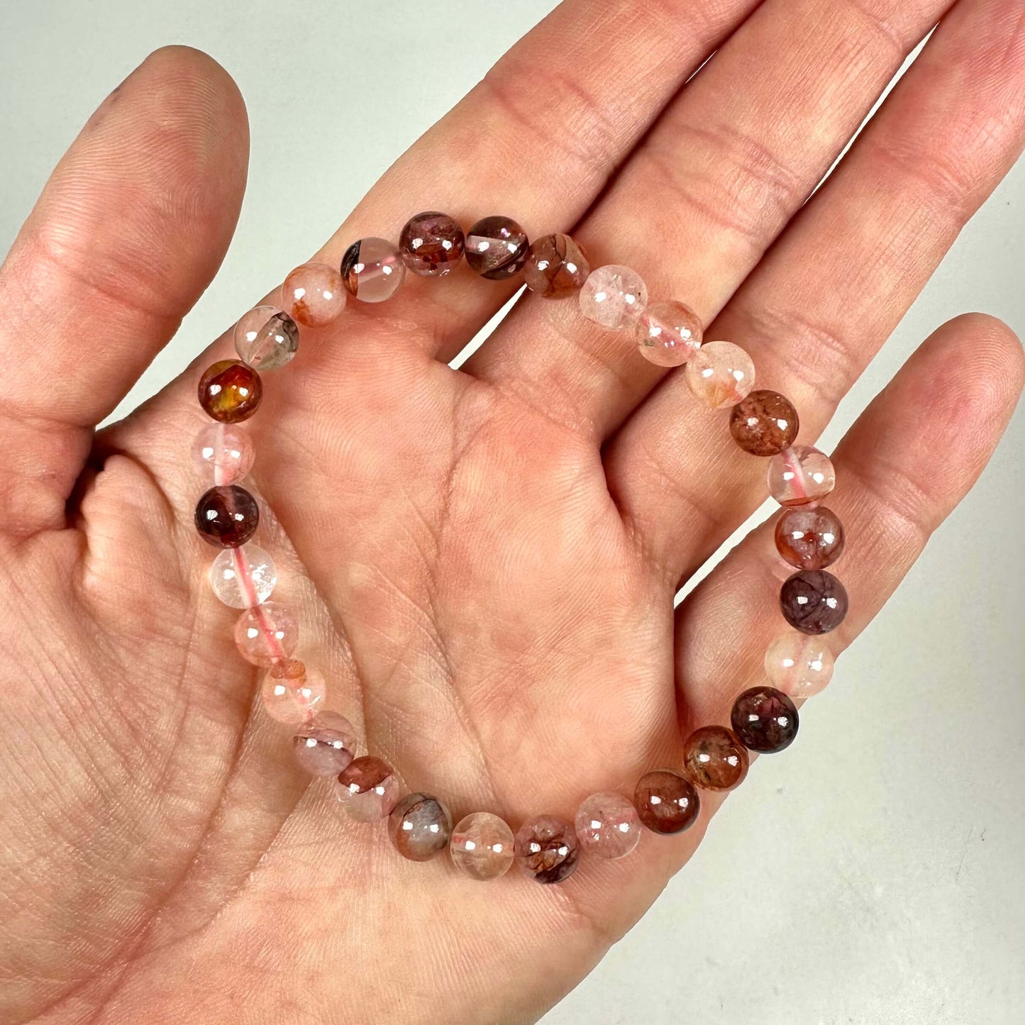 En hånd holder et armbånd med runde perler i forskellige nuancer af rosa og brunt.