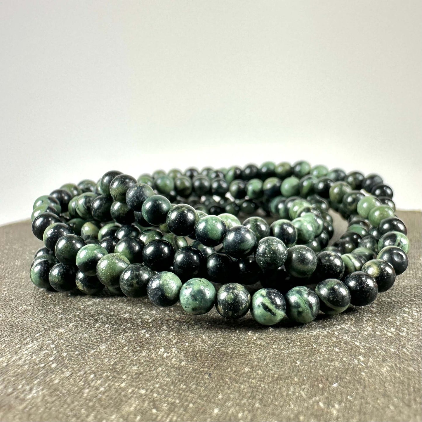 Kæde af grønne og sorte perler arrangeret i en cirkulær form på en lys overflade.