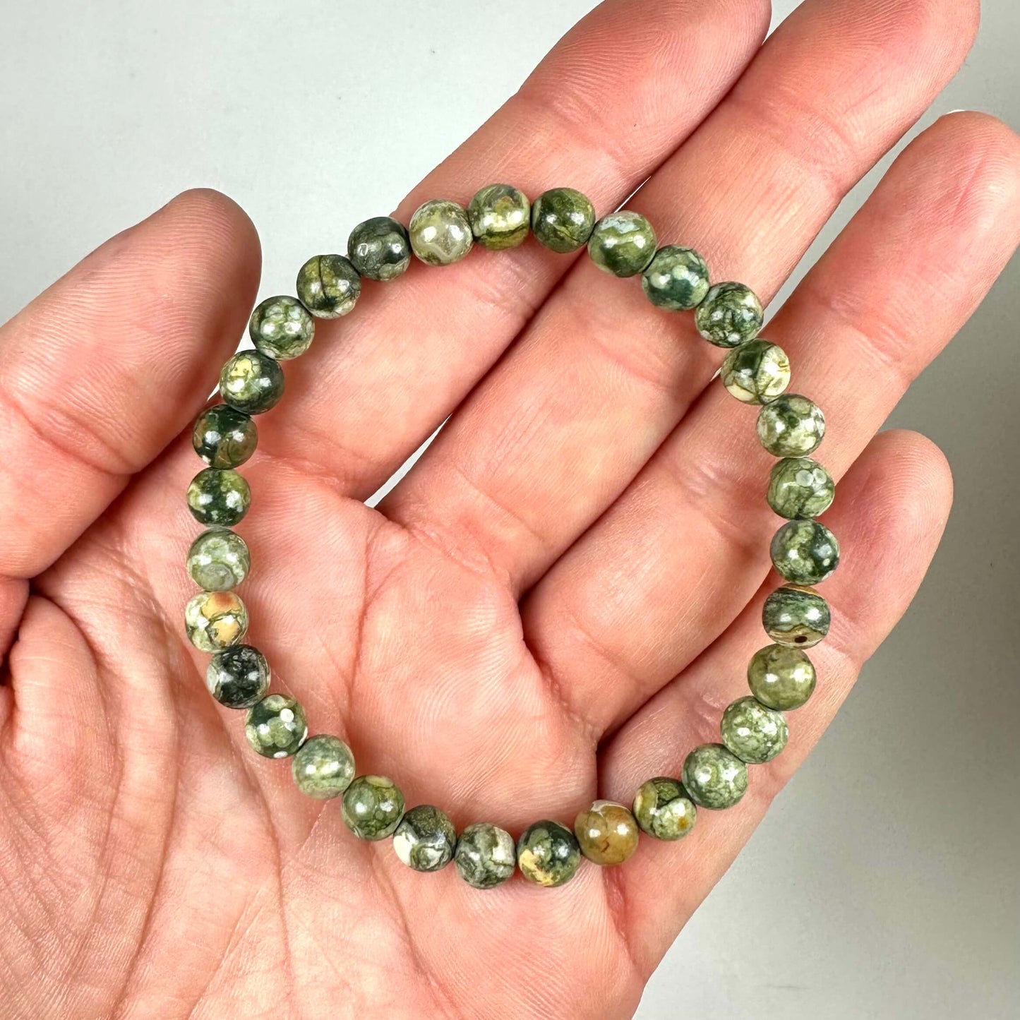 En hånd holder et armbånd med grønne perler i forskellige nuancer.