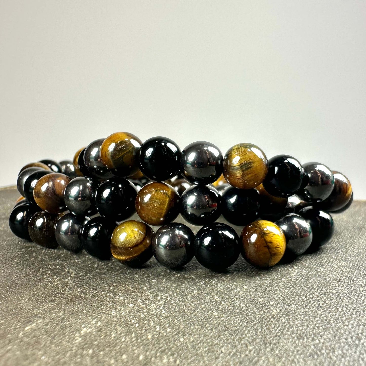 Armbånd med sorte og brune perler arrangeret i cirkler på en mørk teksturoverflade.