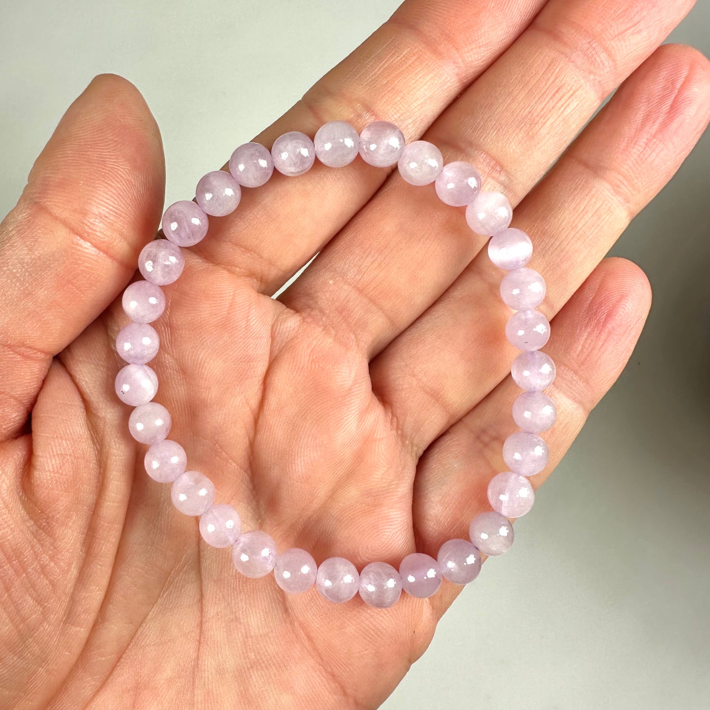 En hånd holder et armbånd lavet af lyserøde perler mod en neutral baggrund.