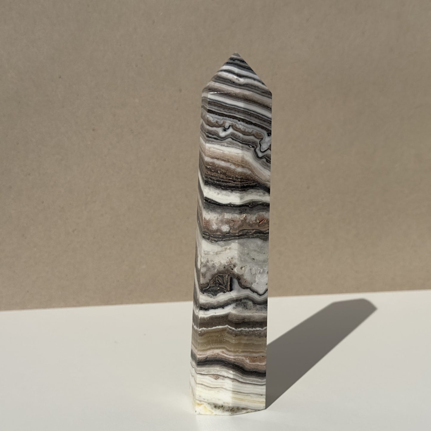 Zebra Calcit tårn nr 4 med lagdelte striber i brune, grå og hvide nuancer på en neutral baggrund.
