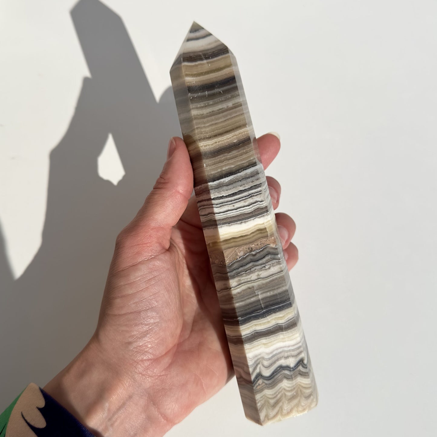 Hånd holder Zebra Calcit tårn nr. 3 med brune og hvide striber mod en lys baggrund.