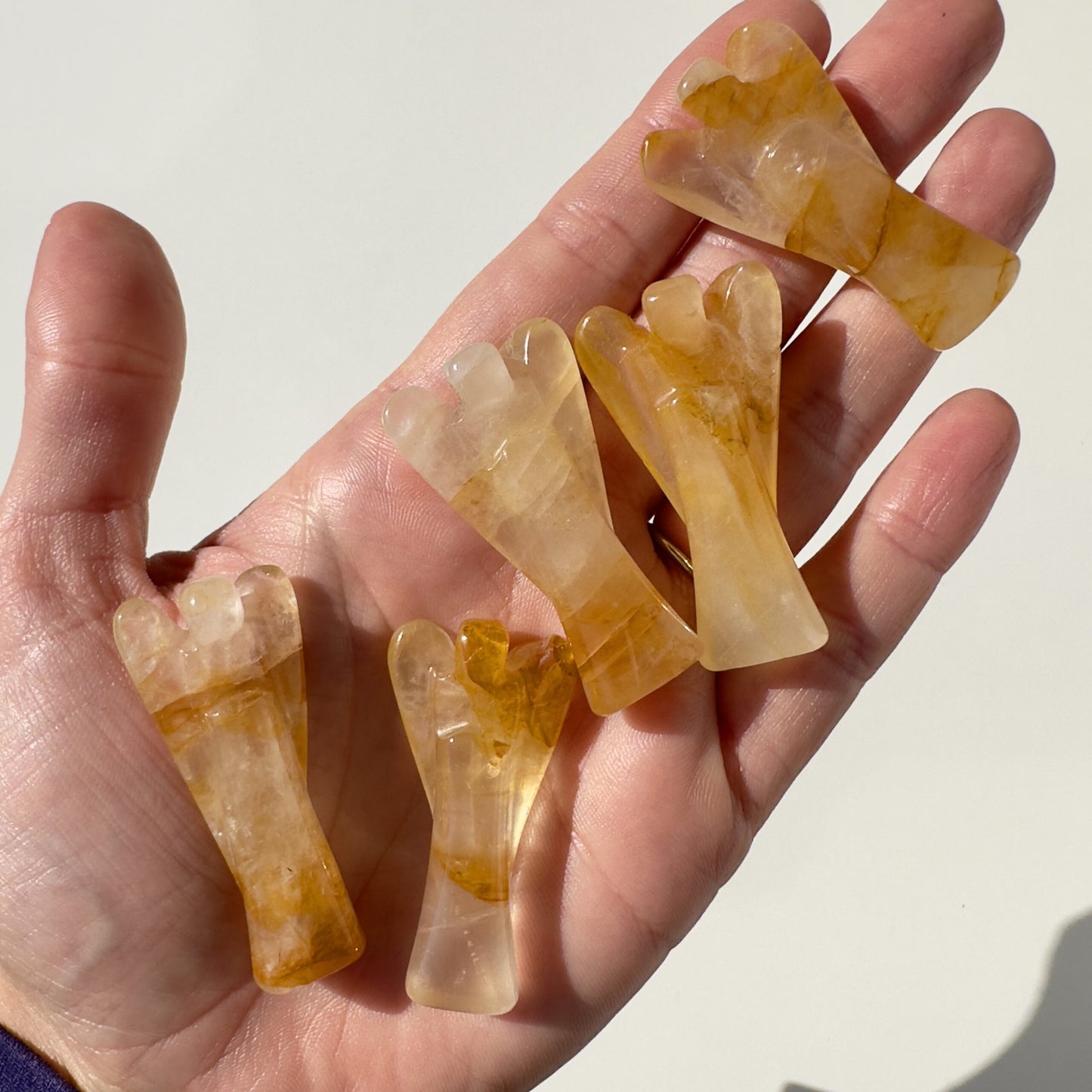 Hånd der holder fem Golden Healer engle udskåret i krystal, belyst af sollys.