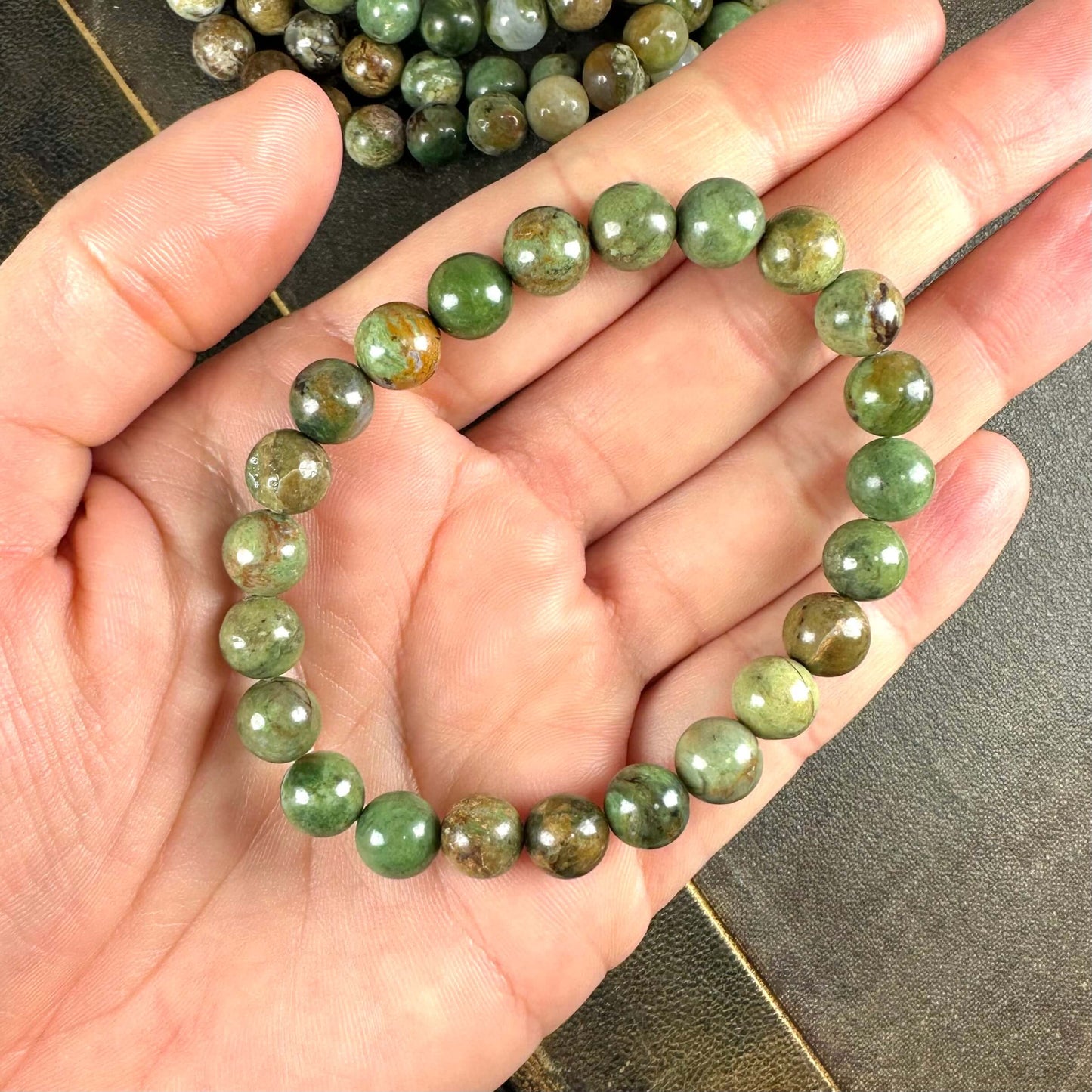 En hånd holder et armbånd med grønne, polerede perler. Armbåndet er cirkelformet og ligger på en åben håndflade.
