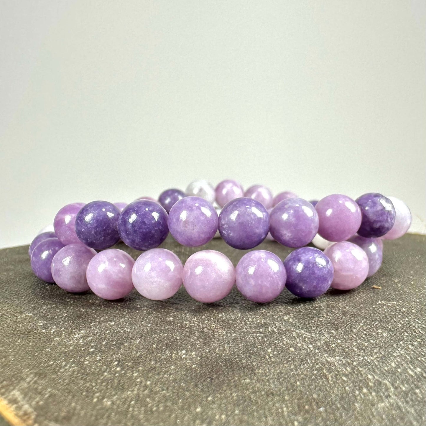To-farvet lilla armbånd af glatte perler lagt på en grå overflade.