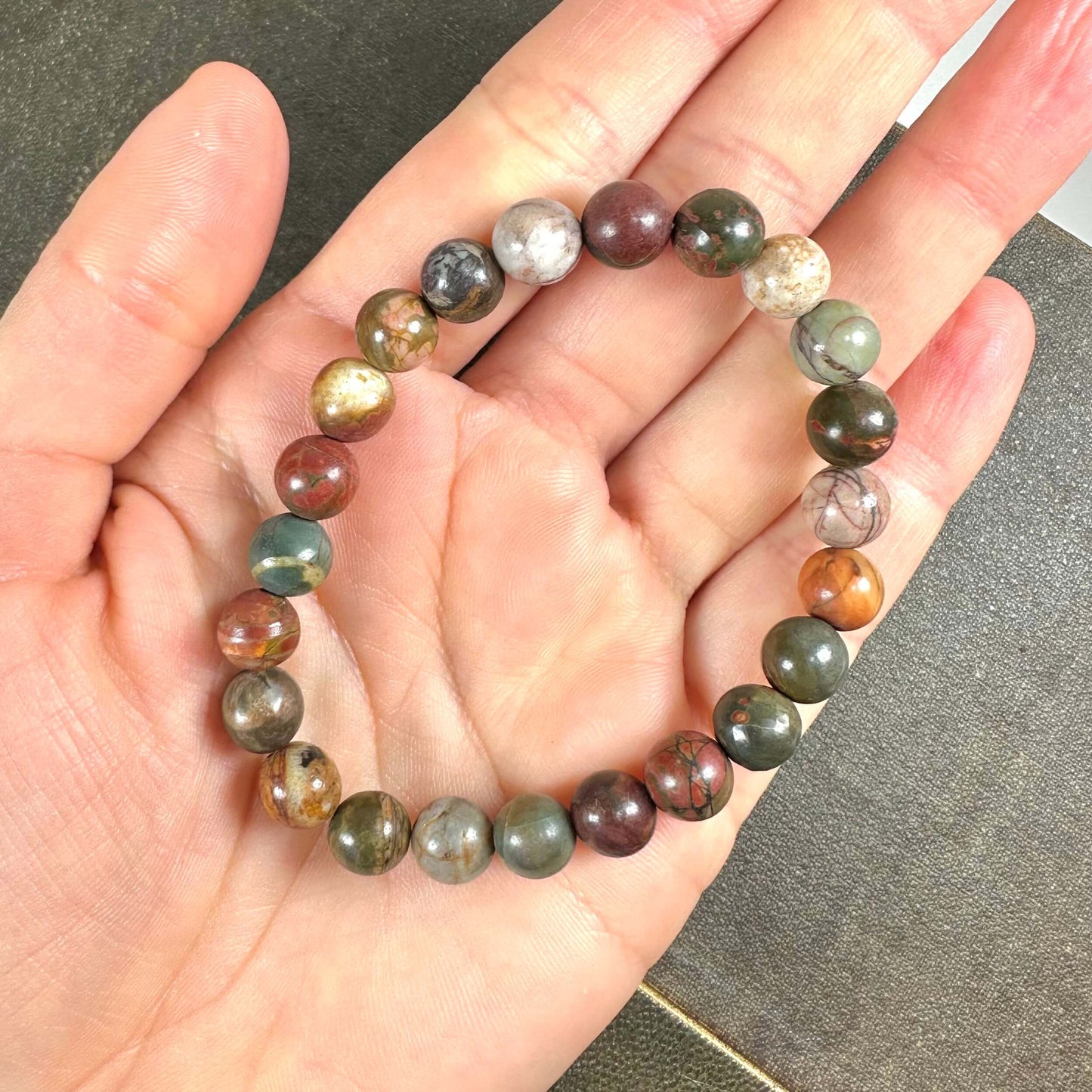 En hånd holder et farverigt armbånd lavet af små stenperler i forskellige nuancer.