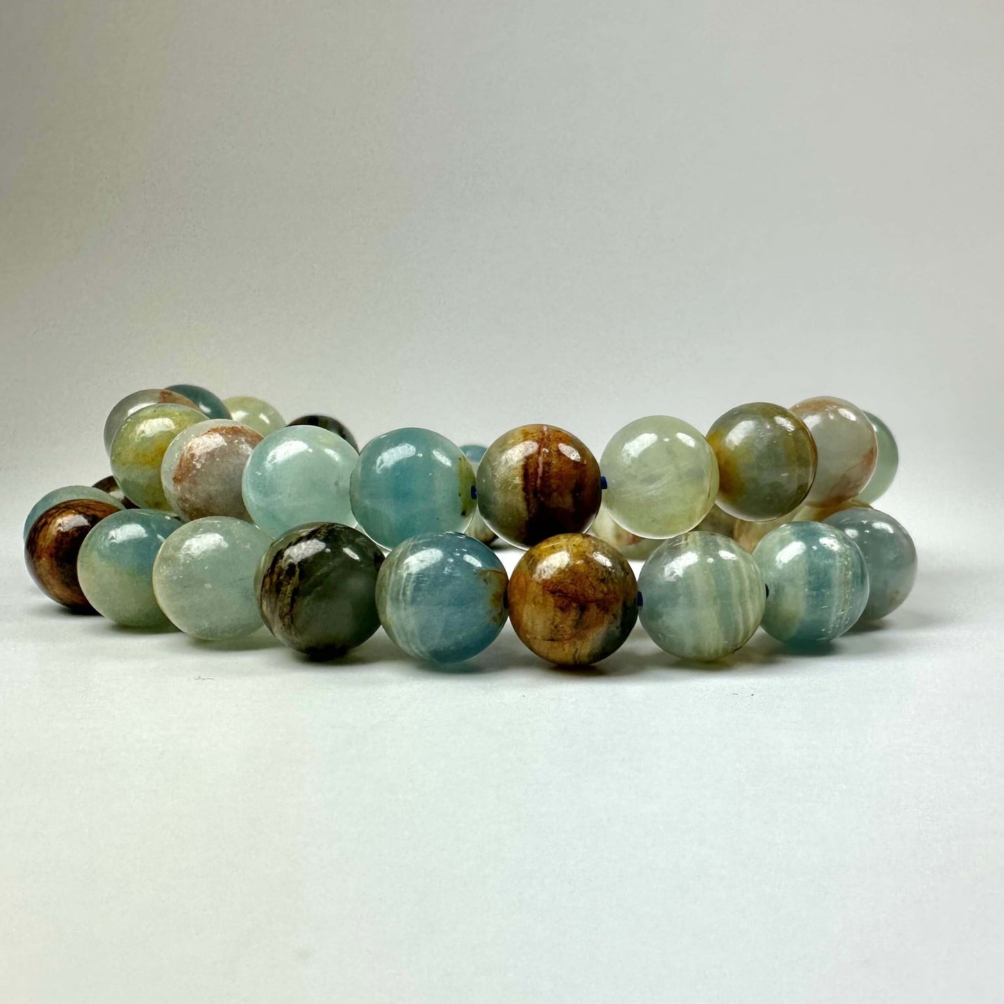 Armbånd med polerede, flerfarvede stenkugler på en neutral baggrund.