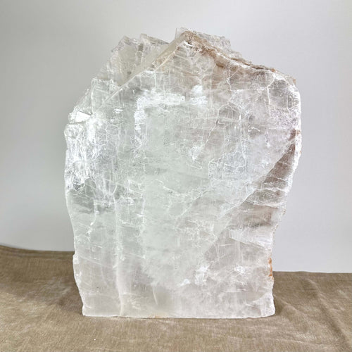 En stor, gennemsigtig bjergkrystal står på en beige overflade med en neutral baggrund.