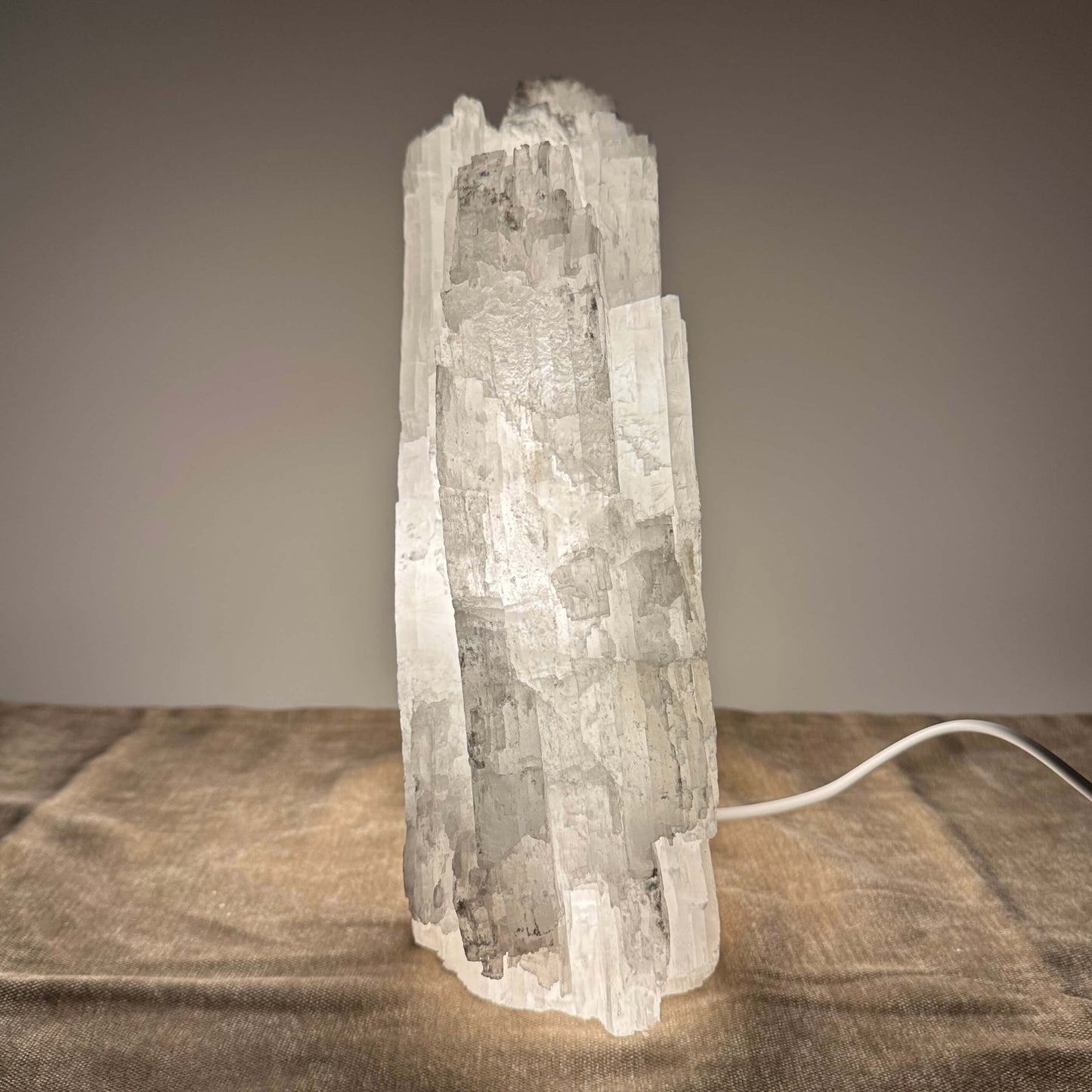 En oplyst selenitkrystal placeret på en brun overflade med en ledning tilsluttet.