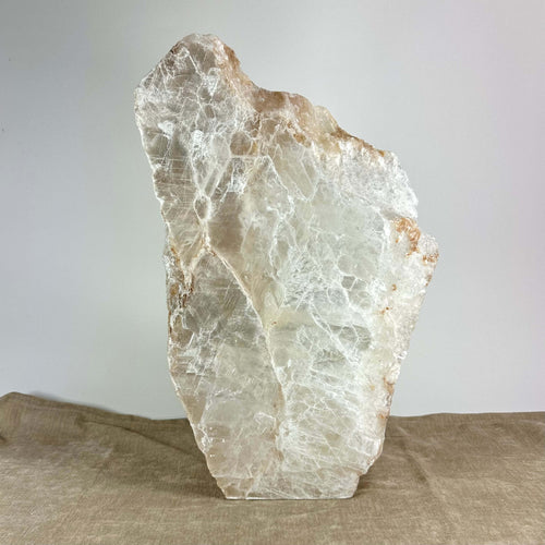 En stor krystalformet sten med hvid og beige farvetoner på en brun overflade.