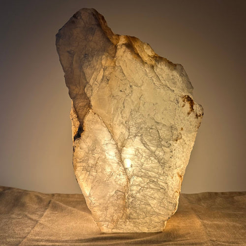 Stor, oplyst sten med ru overflade står på en stofdækket overflade. Skærer mod en simpel, mørk baggrund.