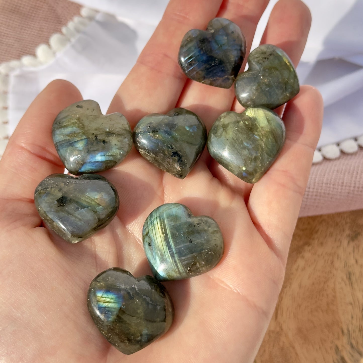 En hånd holder otte skinnende labradorit hjerter mod en lys baggrund.