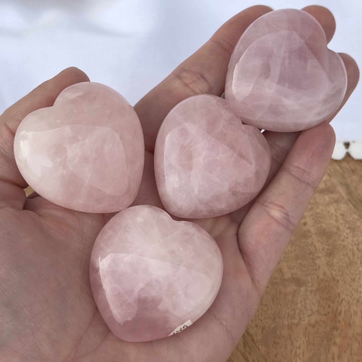 En hånd holder fire rosenkvarts hjerter, som er blankpolerede og lyserøde.