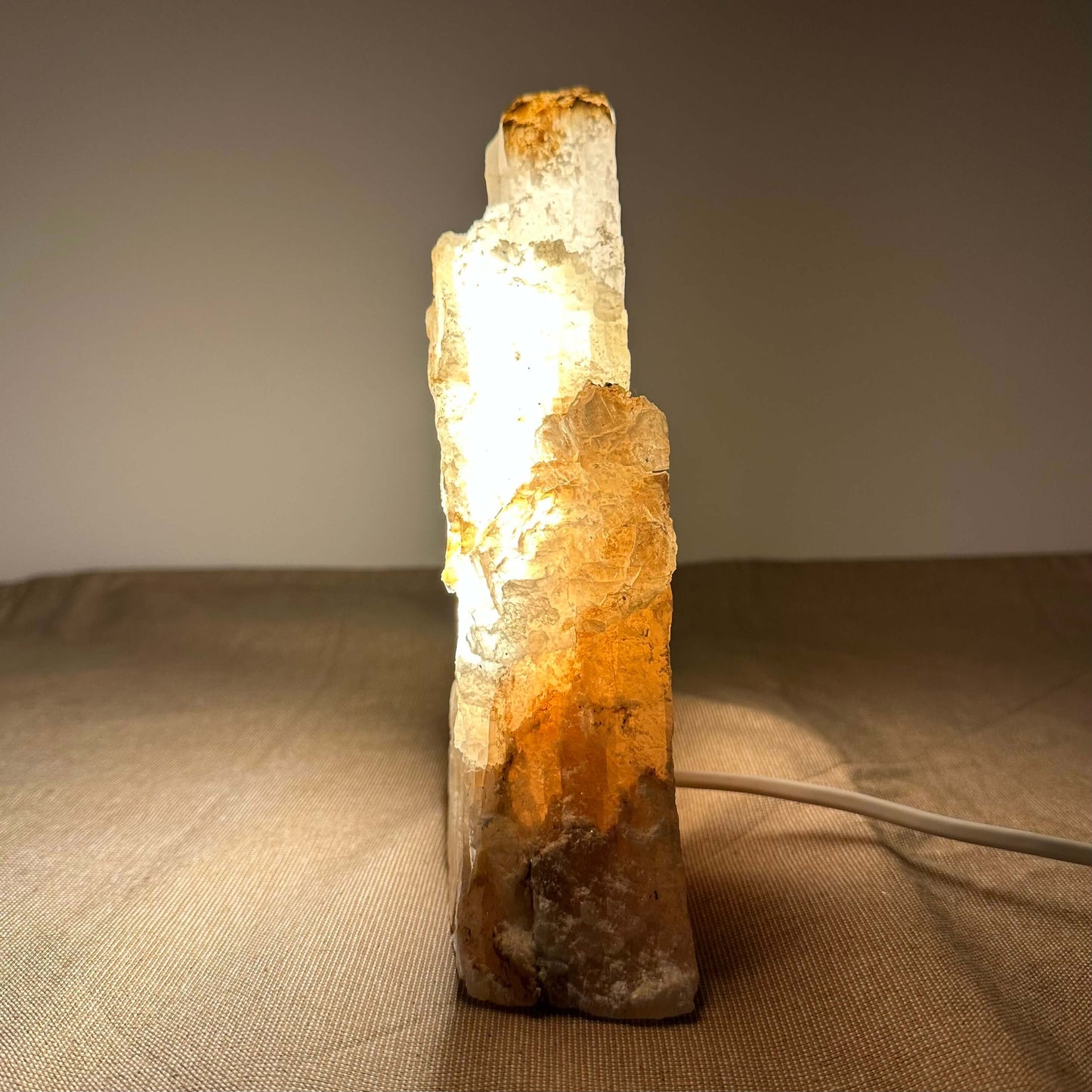 En oplyst krystallampe med orange nuancer står på et bord med en lys ledning bagved.