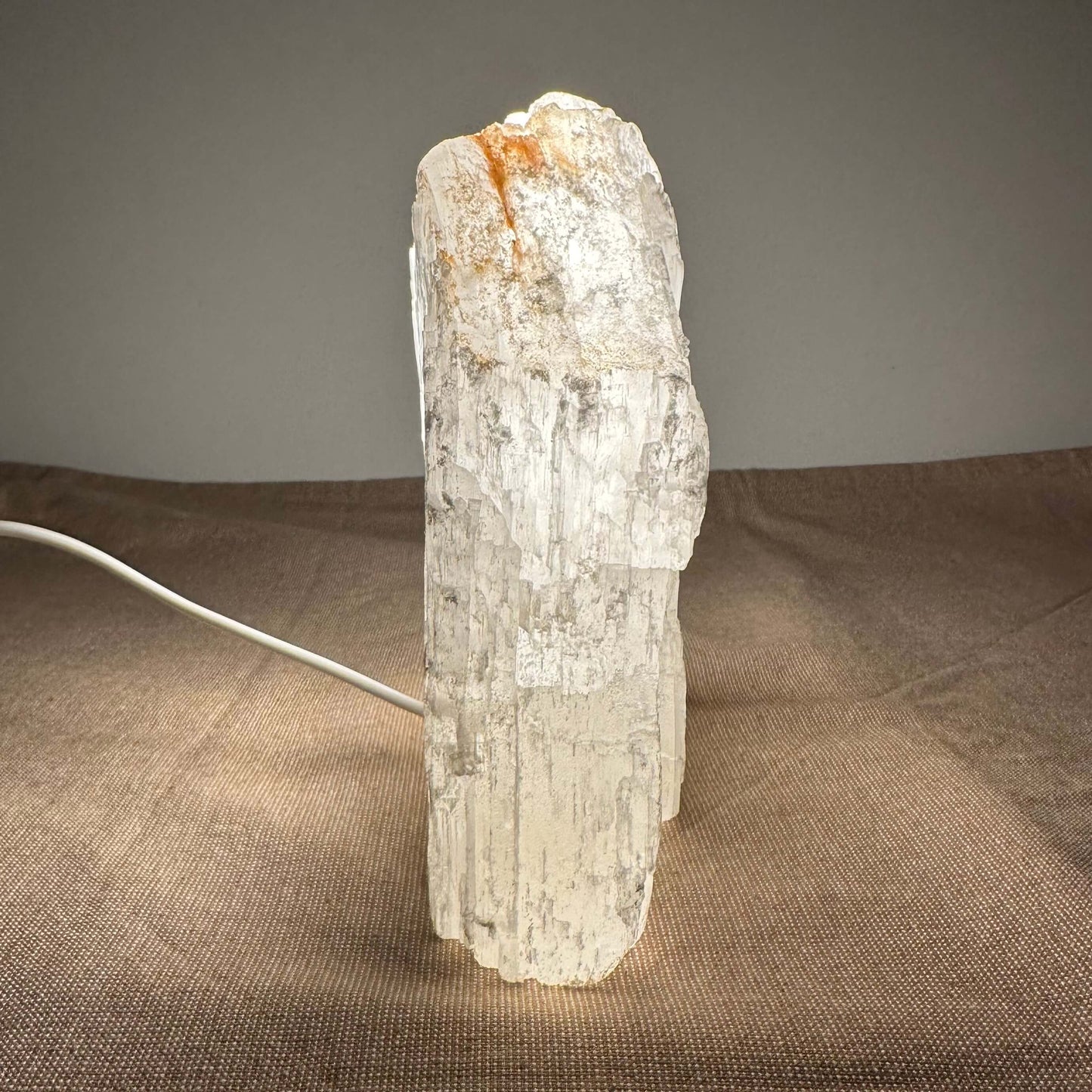 En oplyst selenit-lampe på et bord med brun dug.