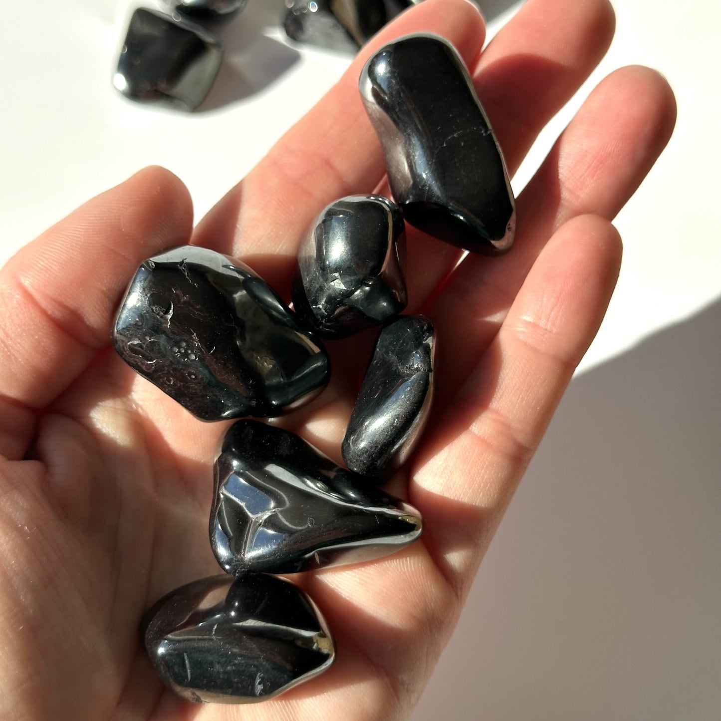 Håndfuld af glatte, sorte hæmatit lommesten i en åben håndflade, belyst af sollys.