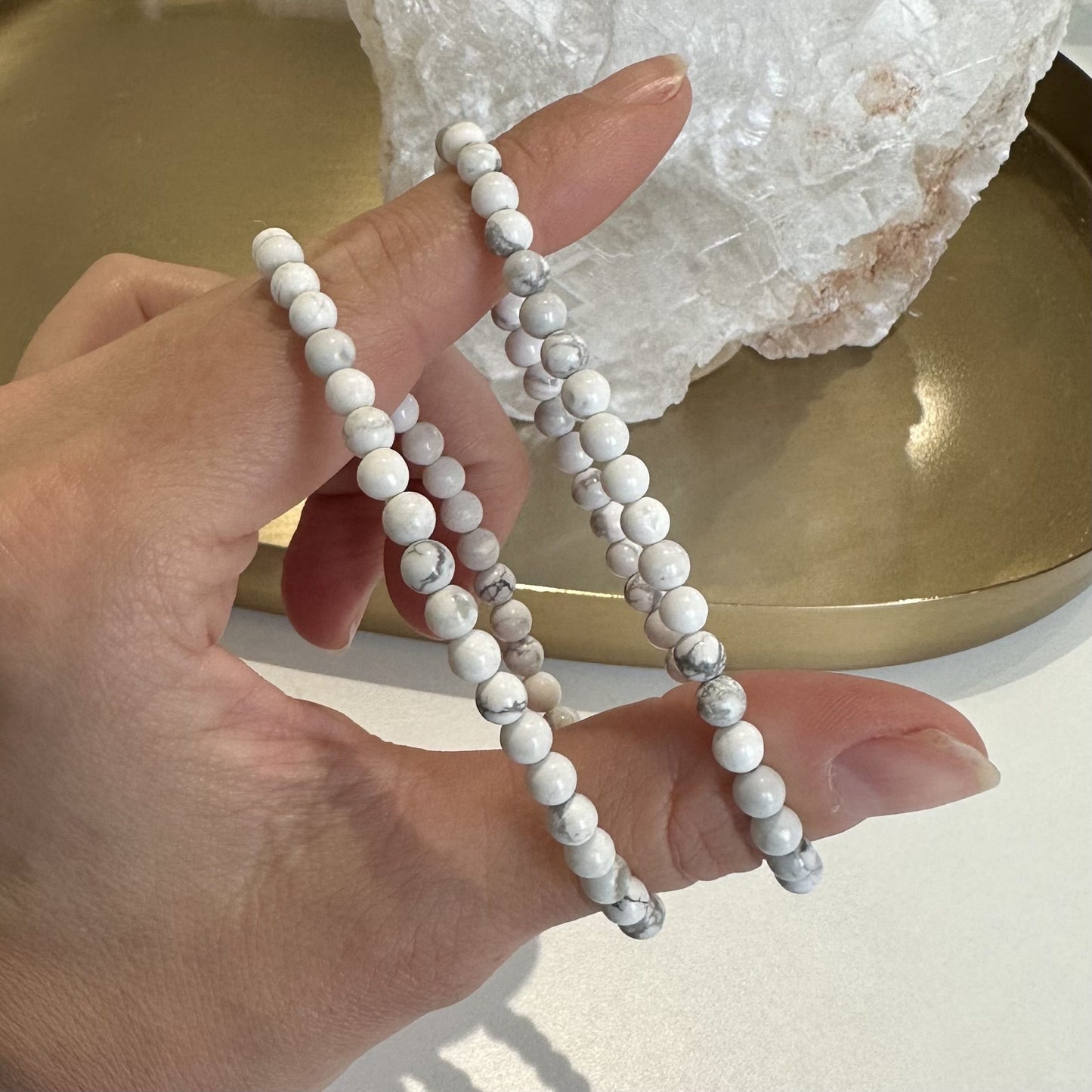 Hånd med to Howlit perle armbånd foran en krystal på en guldbakke.