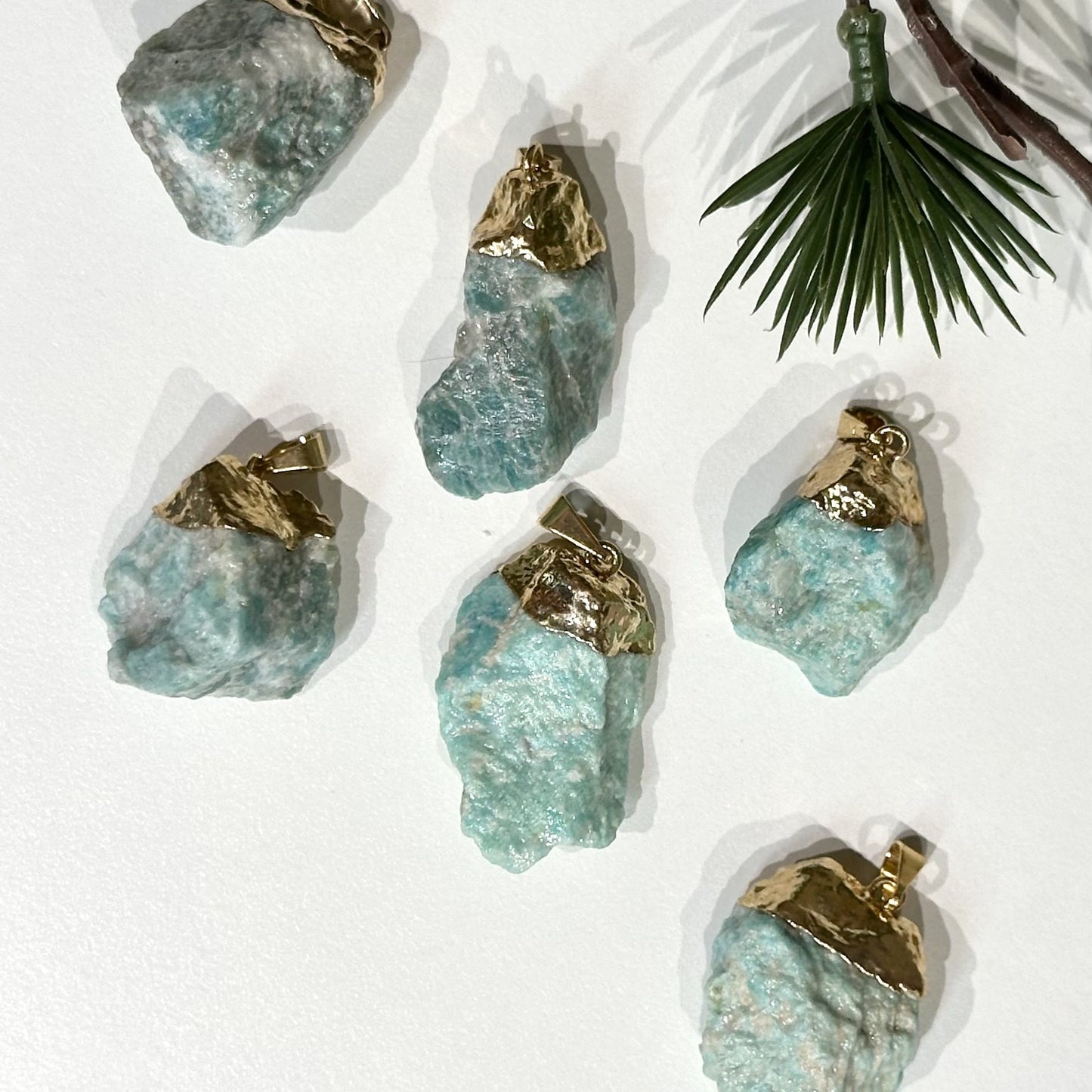 Amazonit ophæng 3 stk med gyldne toppe på lys baggrund, omgivet af en grøn plantegren.