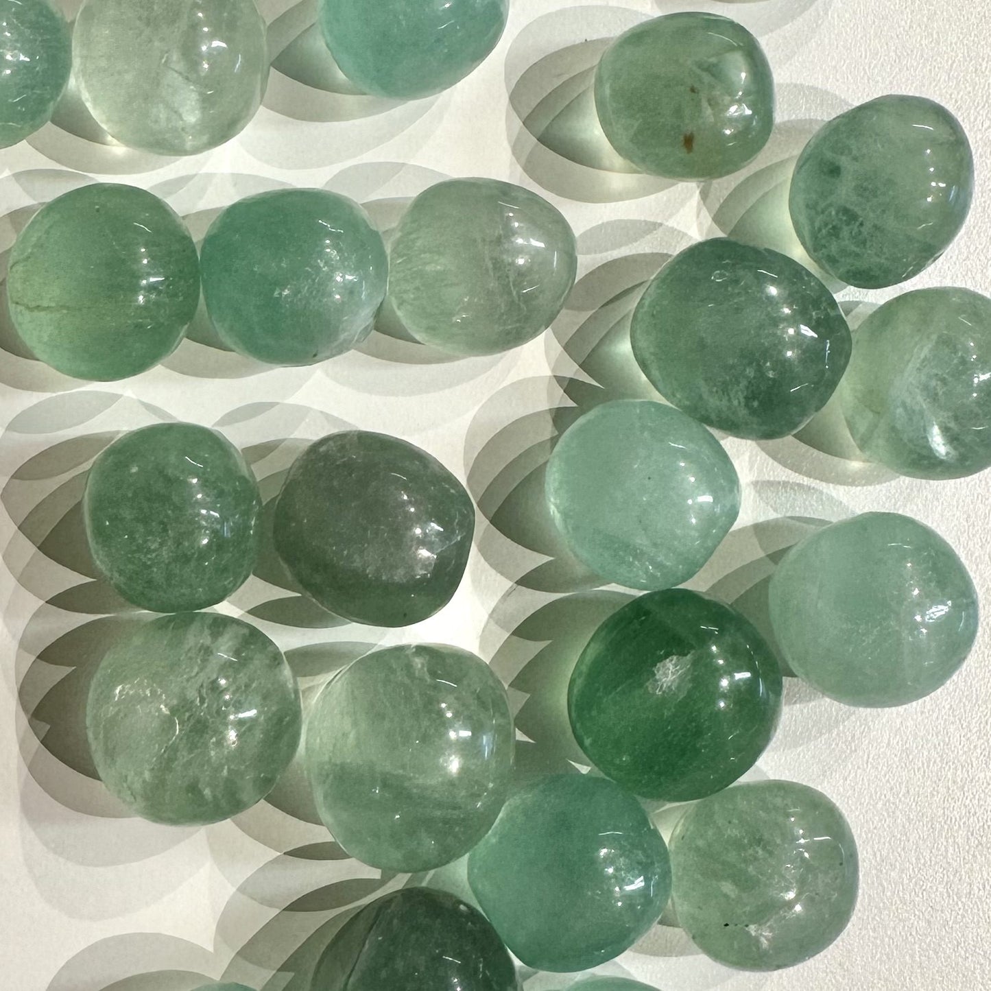 Fluorit lommesten i forskellige nuancer af grønne nuancer, spredt på en hvid overflade.