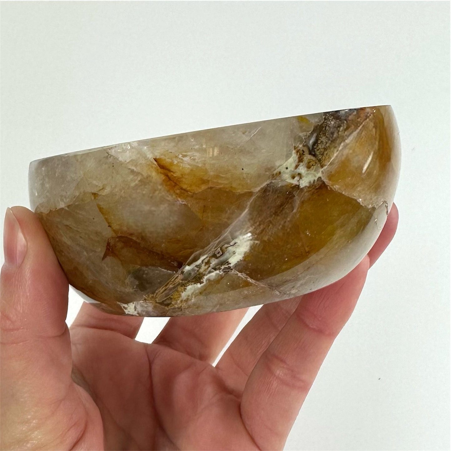 Hånd holder en gylden healer skål med brunlige og hvide nuancer mod en lys baggrund.