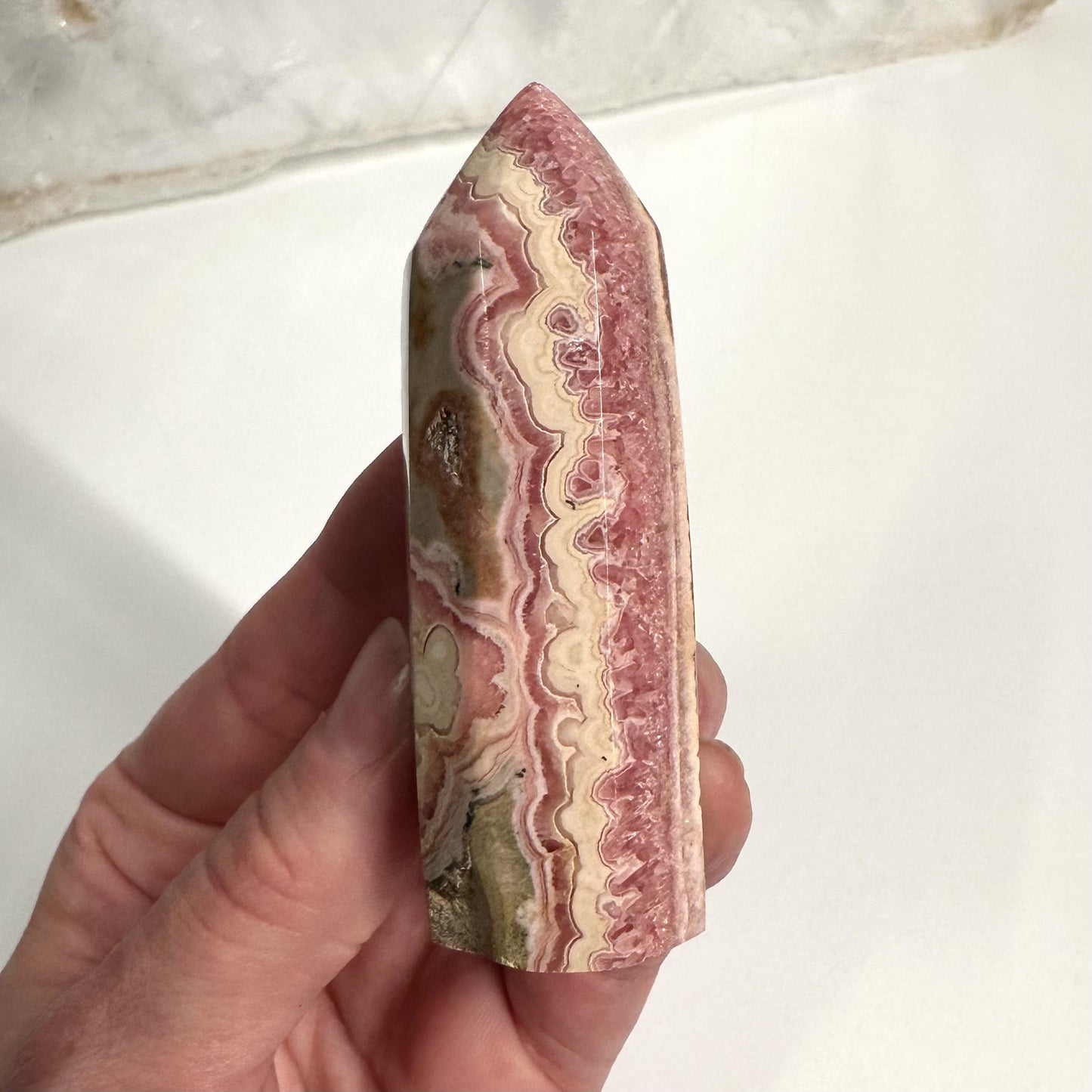Hånd holder Rhodocrosit tårn | eksklusiv kvalitet, med rosa, hvid og beige bånd.