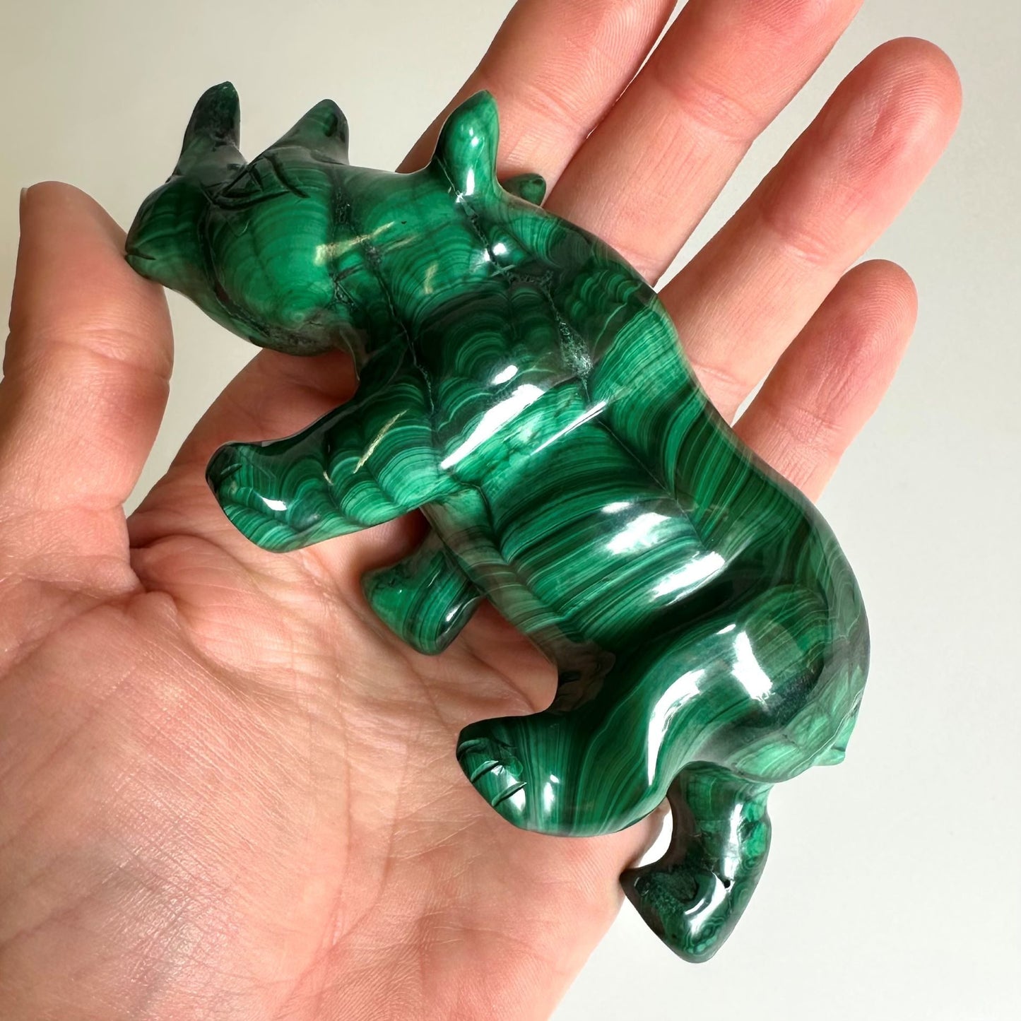 Malakit næsehornsfigur i en hånd, med detaljerede striber i grønt og sort stenmateriale.