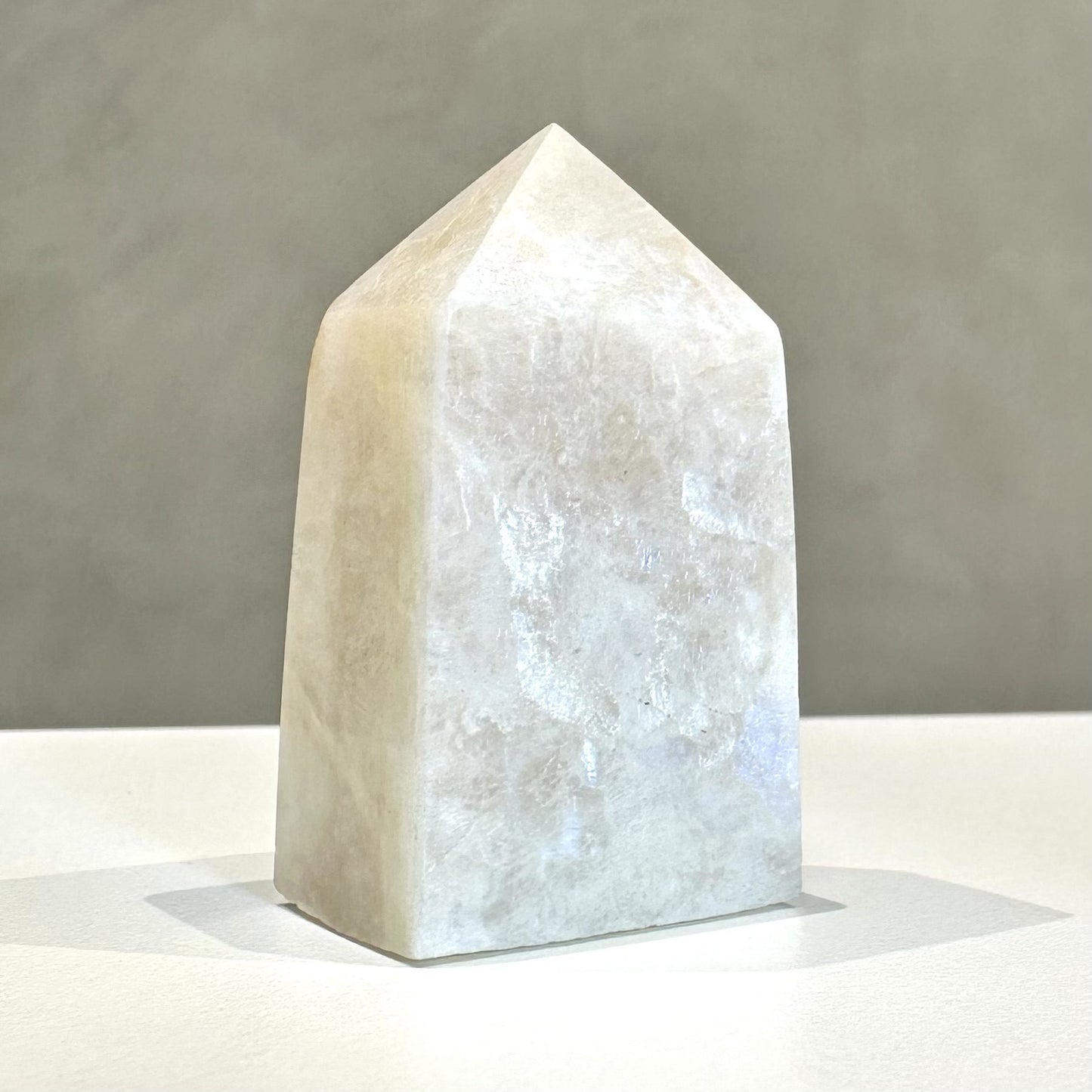 Regnbue Månesten tårn med lysglans, står på en lys overflade mod en grå baggrund.