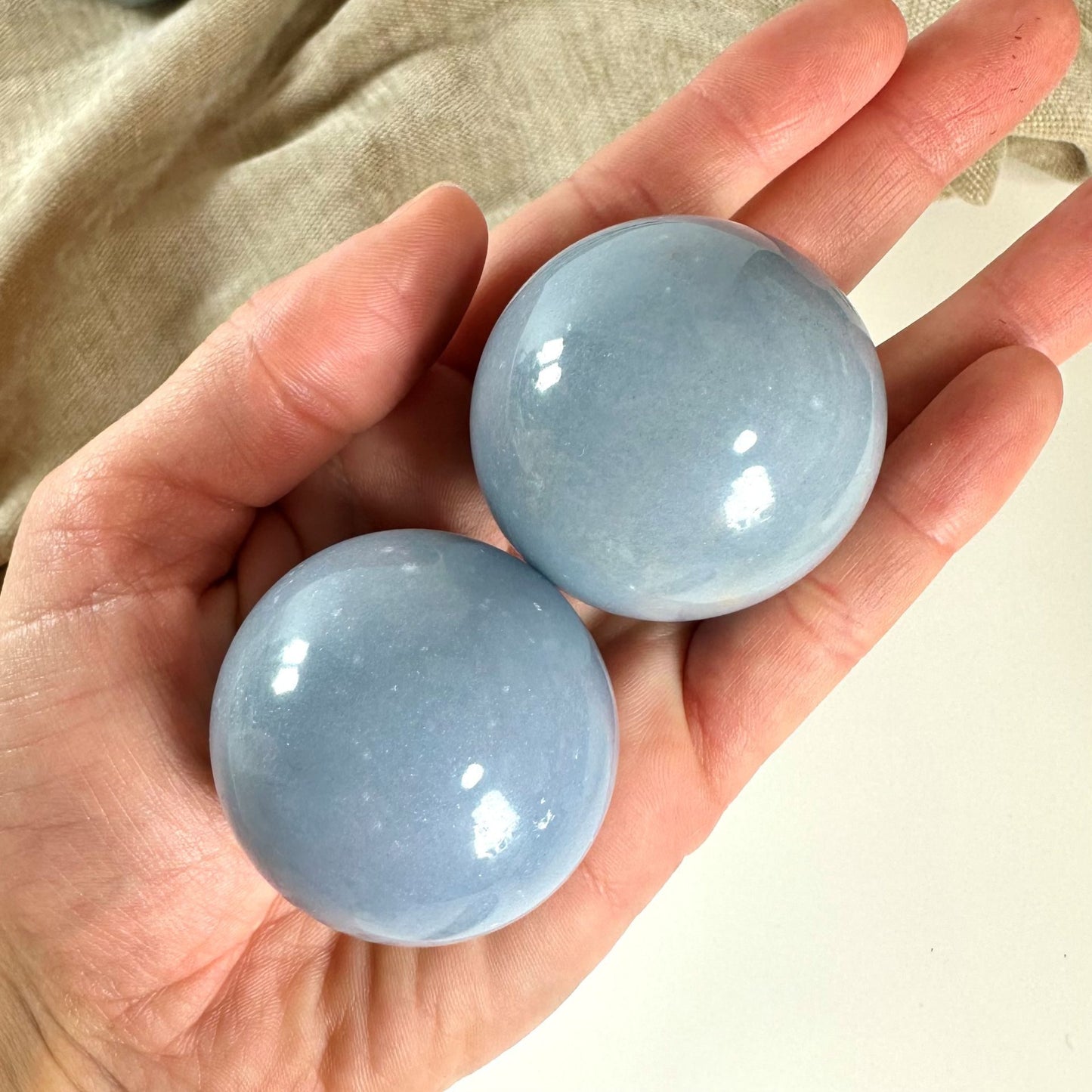 Hånd holder to glatte Angelit kugler mod en beige baggrund.