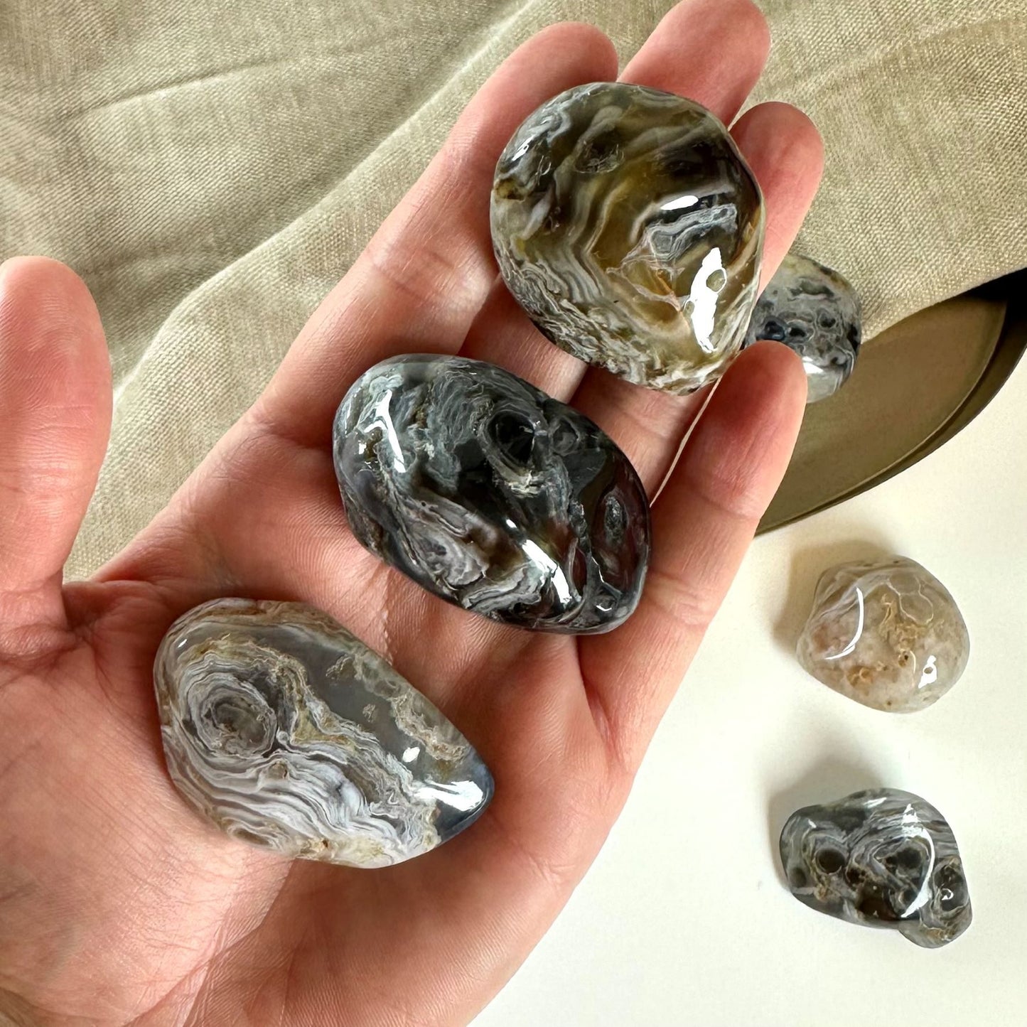 En hånd, der holder flere agat fjer lommesten på en baggrund af tekstil. Andre sten ses på bordet.