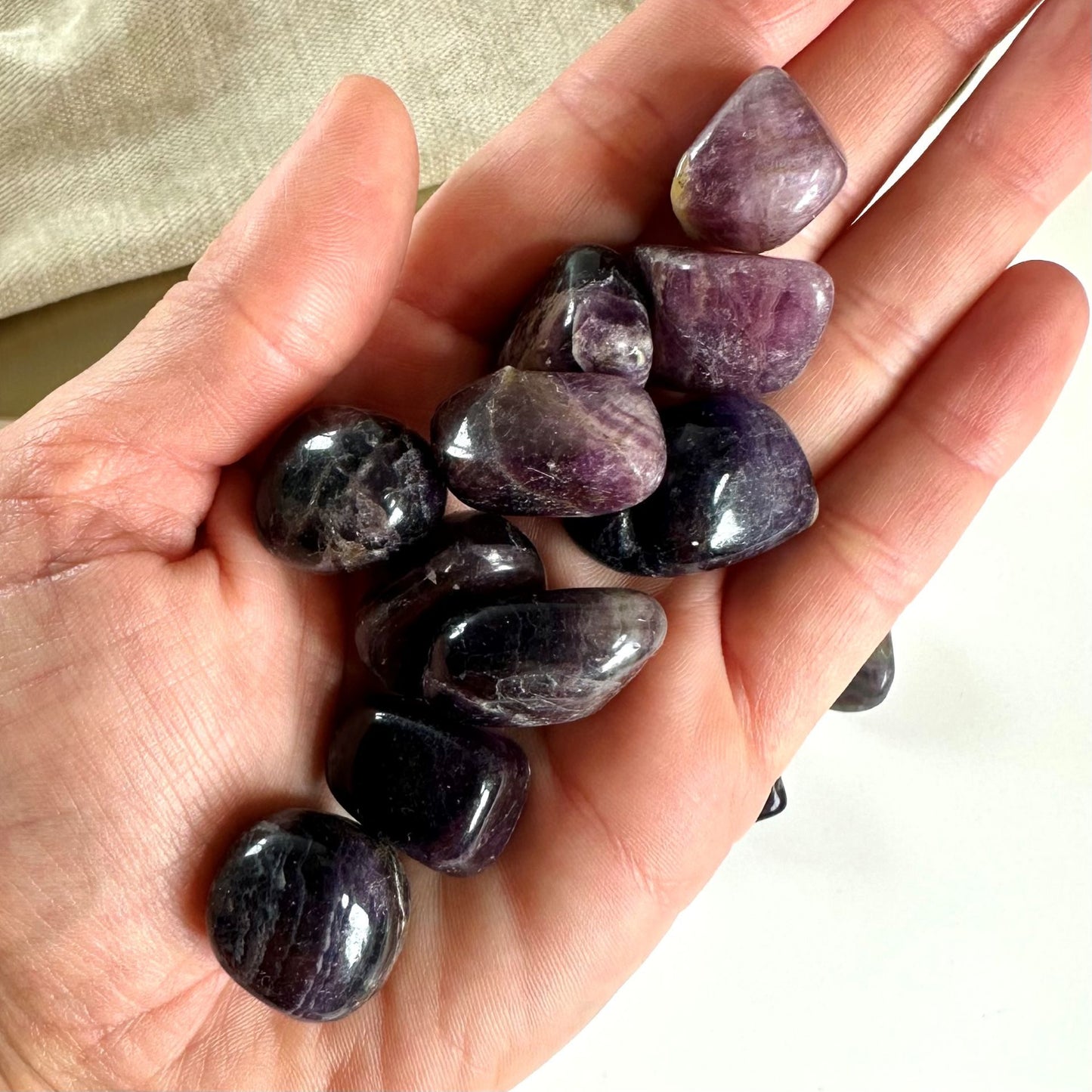 En hånd holder flere glatte, lilla Fluorit lommesten mod en lys baggrund.