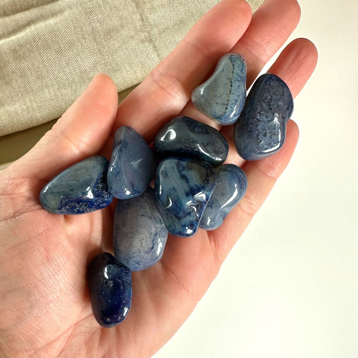 Hånd med glatte, blå agatsten mod en lys baggrund.