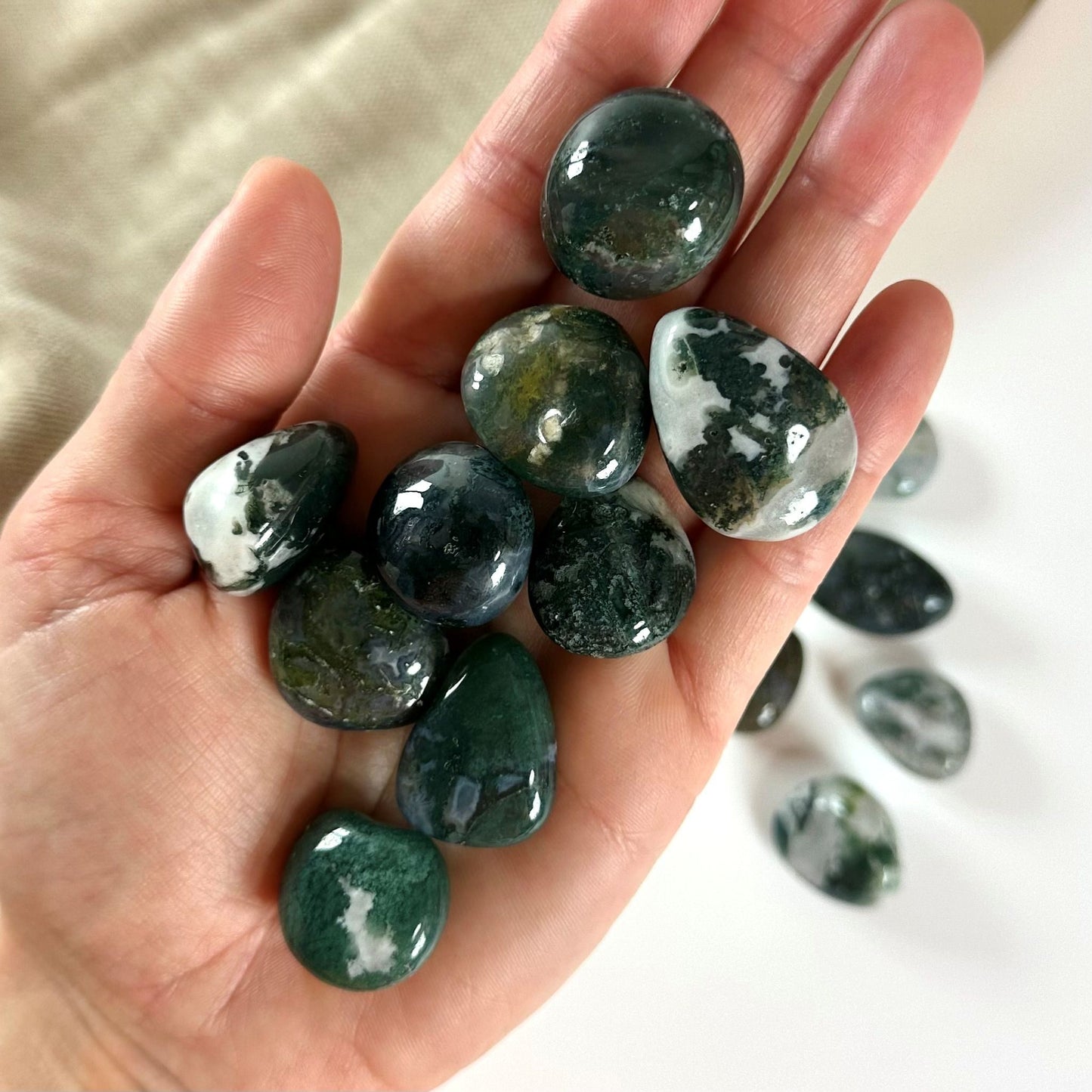Håndfuld af Mos Agat lommesten med grønne og hvide nuancer, liggende i en åben håndflade.