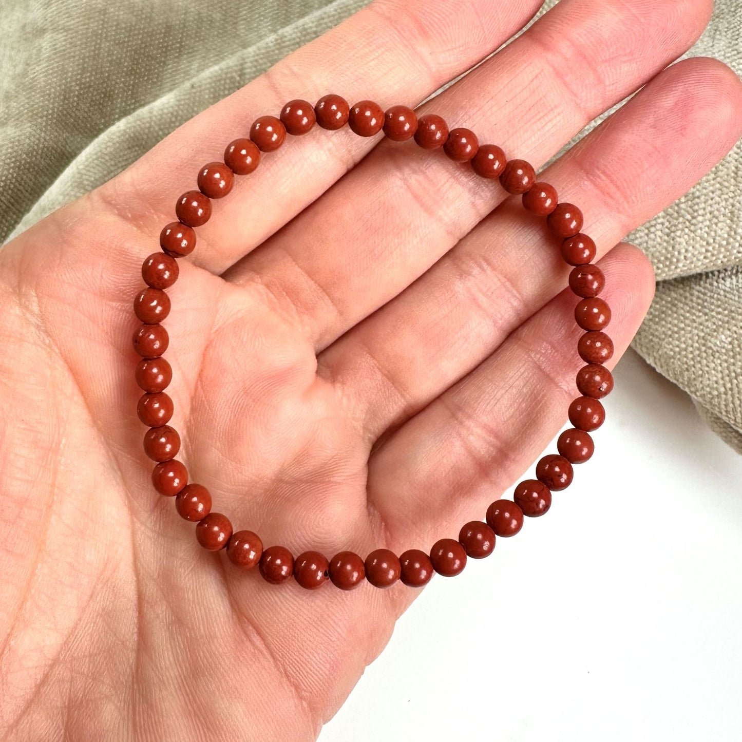 En Rød Jaspis armbånd af perler holdt i en hånd, med en beige baggrund.