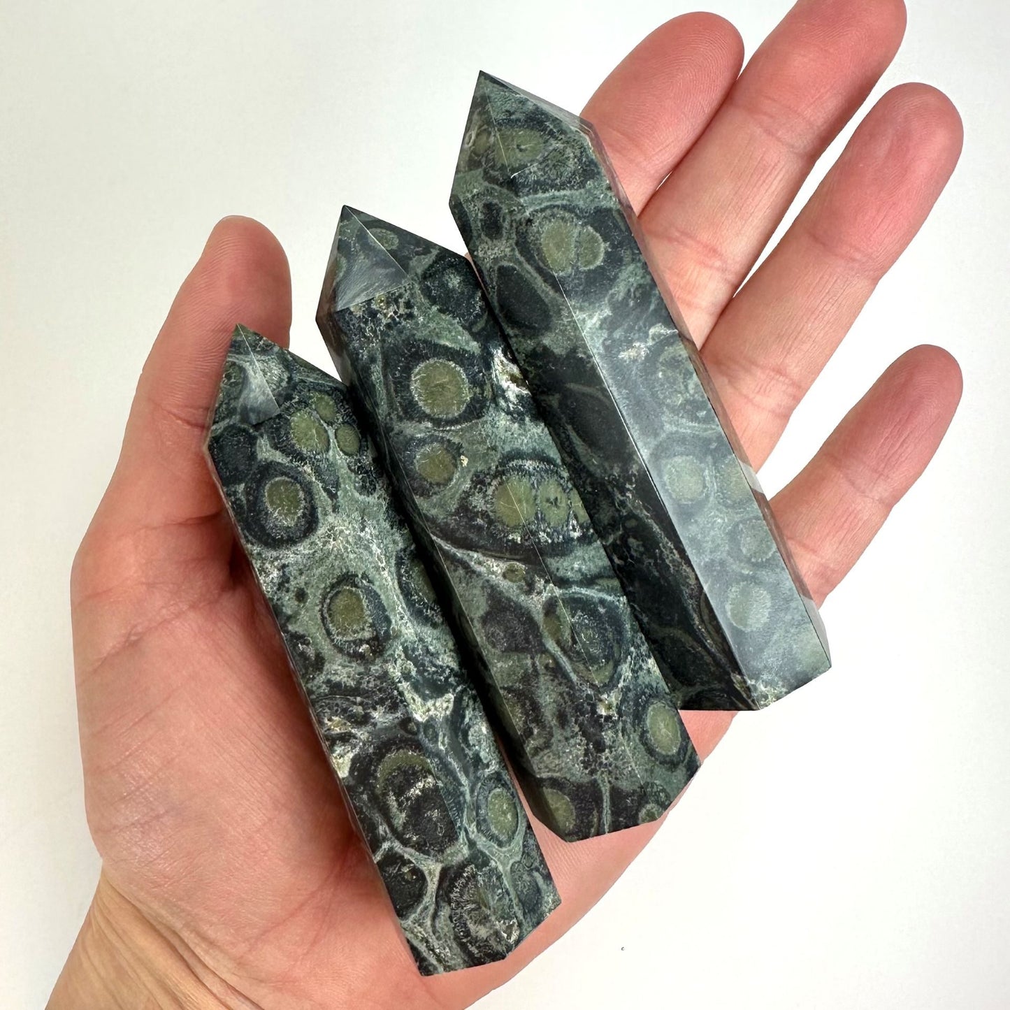 Hånd holder tre Jaspis Kabamba tårne med unikke mønstre og grønne toner.
