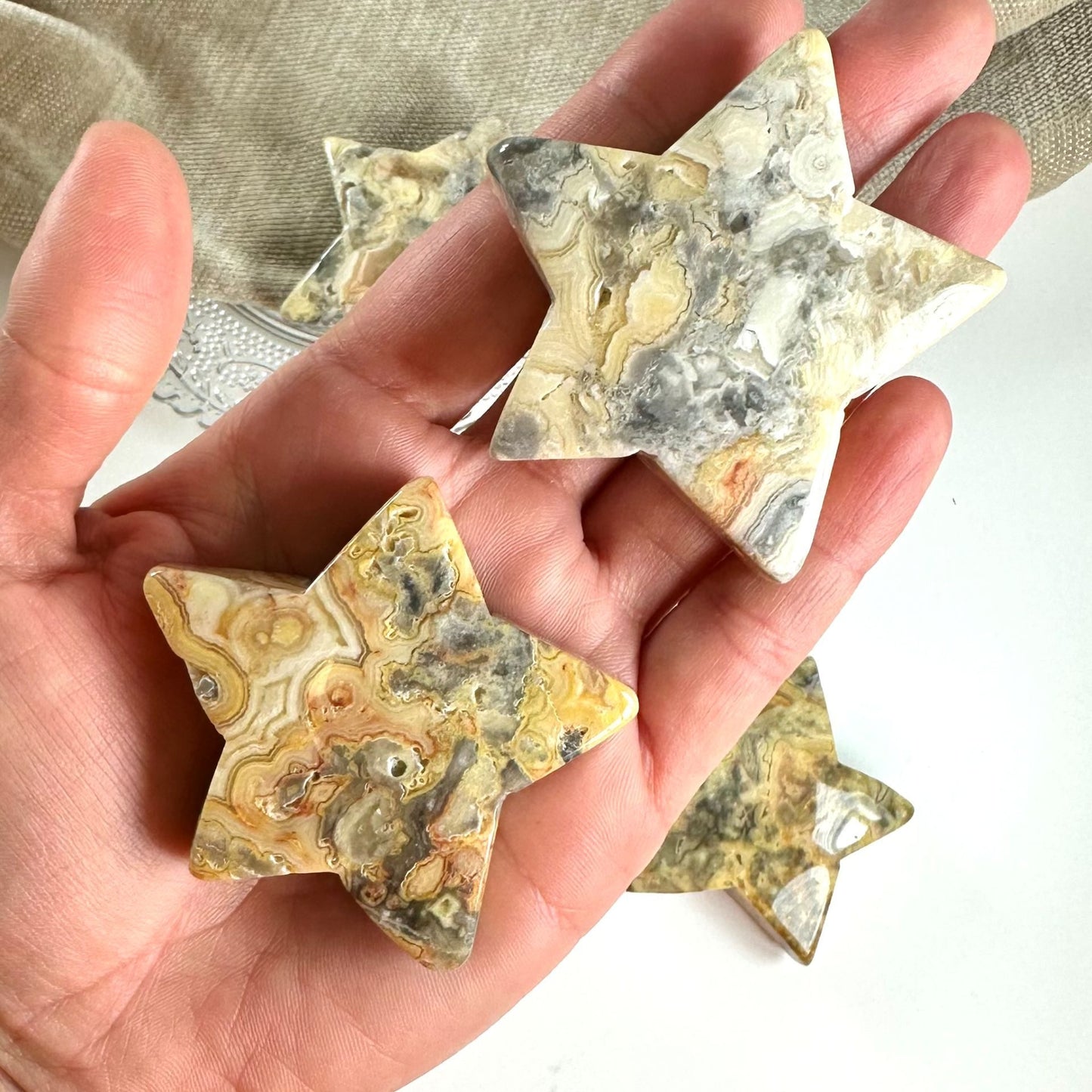 Hånd holder Agat crazy lace stjerner med detaljeret mønster i brune, grå og gule nuancer.