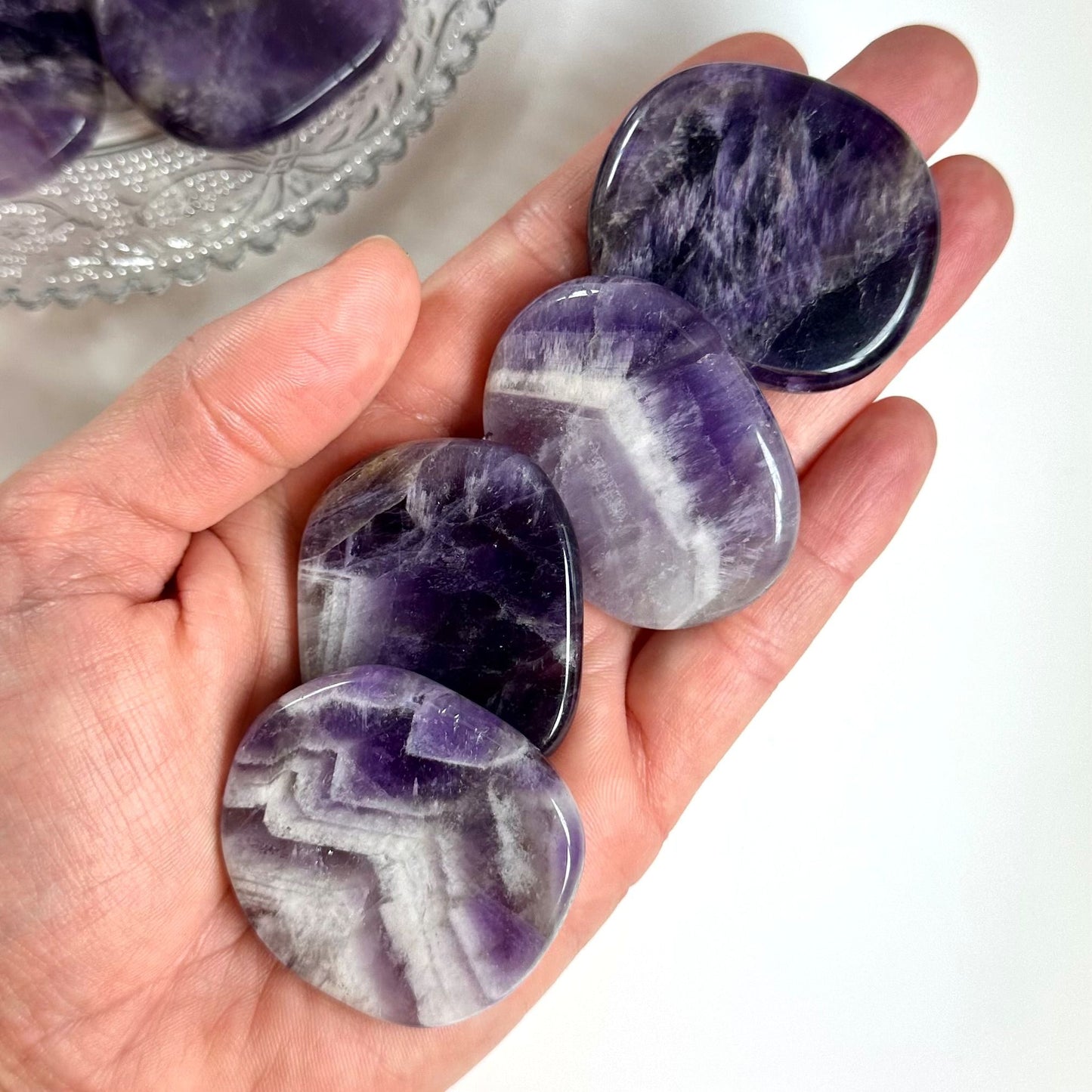 Hånd holder glatte skiver af ametyst med lilla og hvide mønstre.