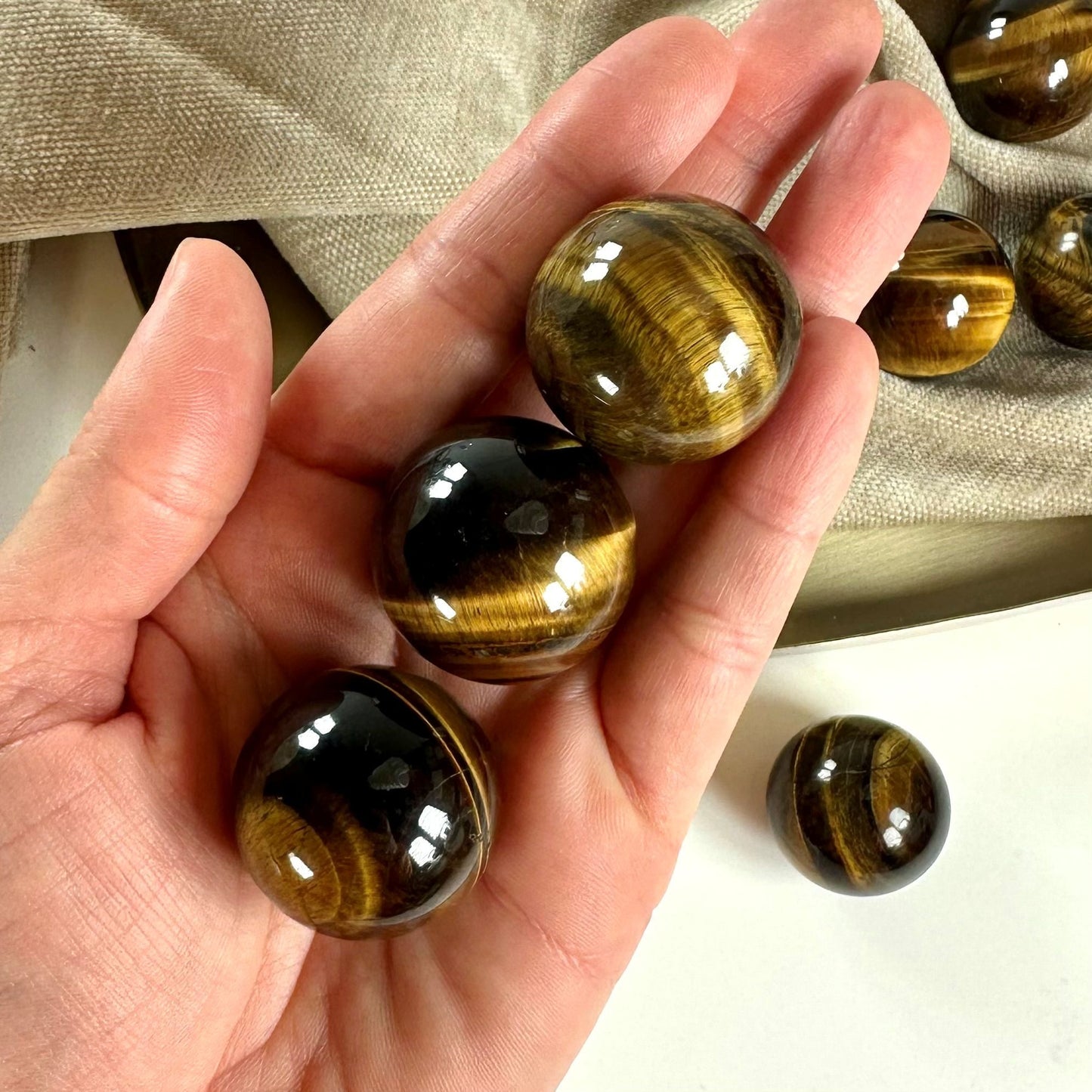 En hånd holder flere Tigerøje kugler med brune og gule striber på en lys baggrund.