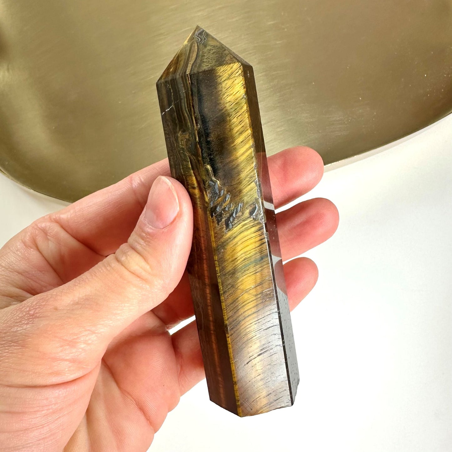 En hånd holder et poleret Tigerøje tårn mod en lys baggrund.