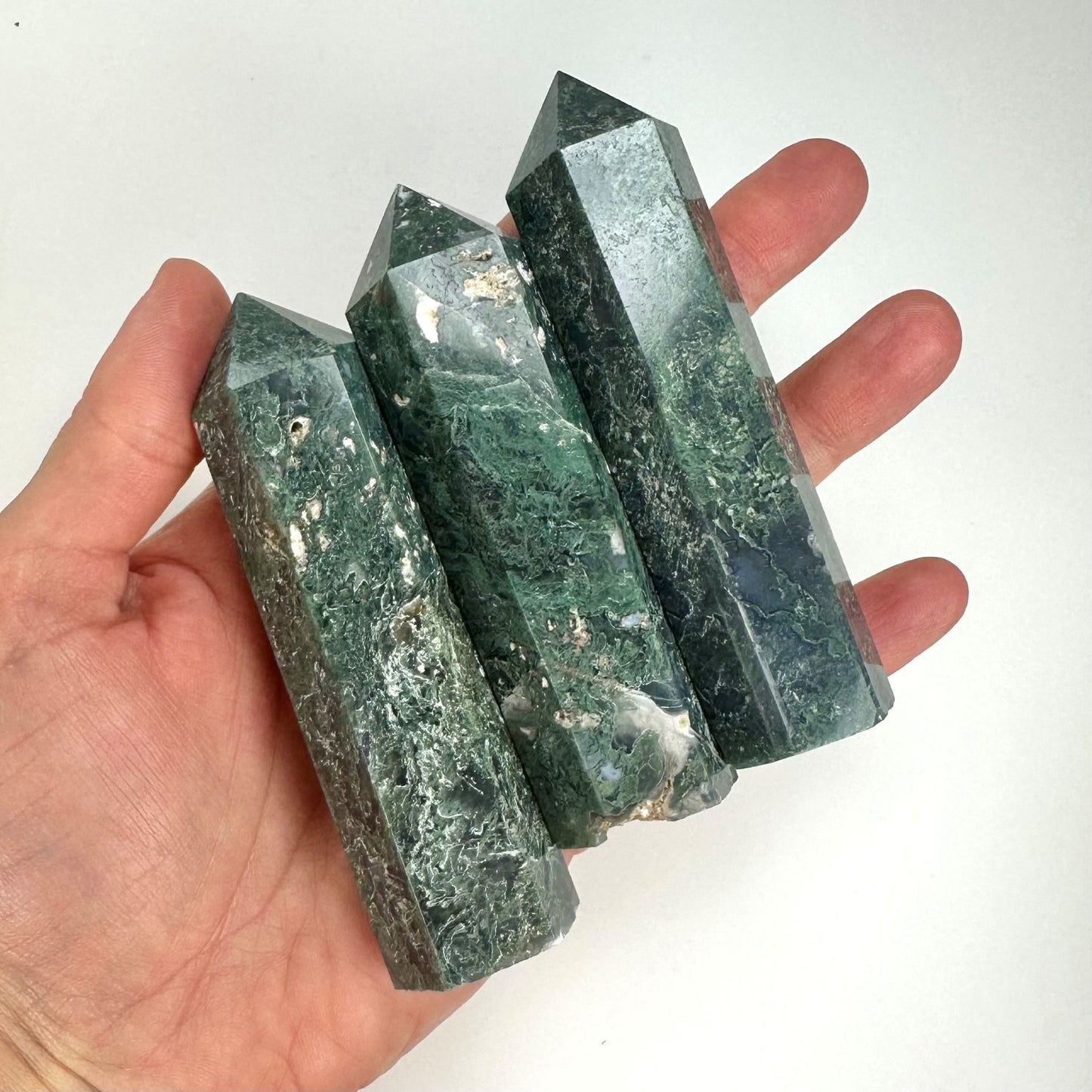 Hånd holder tre grønne Mos Agat tårn med tydelig tekstur og krystallstruktur.