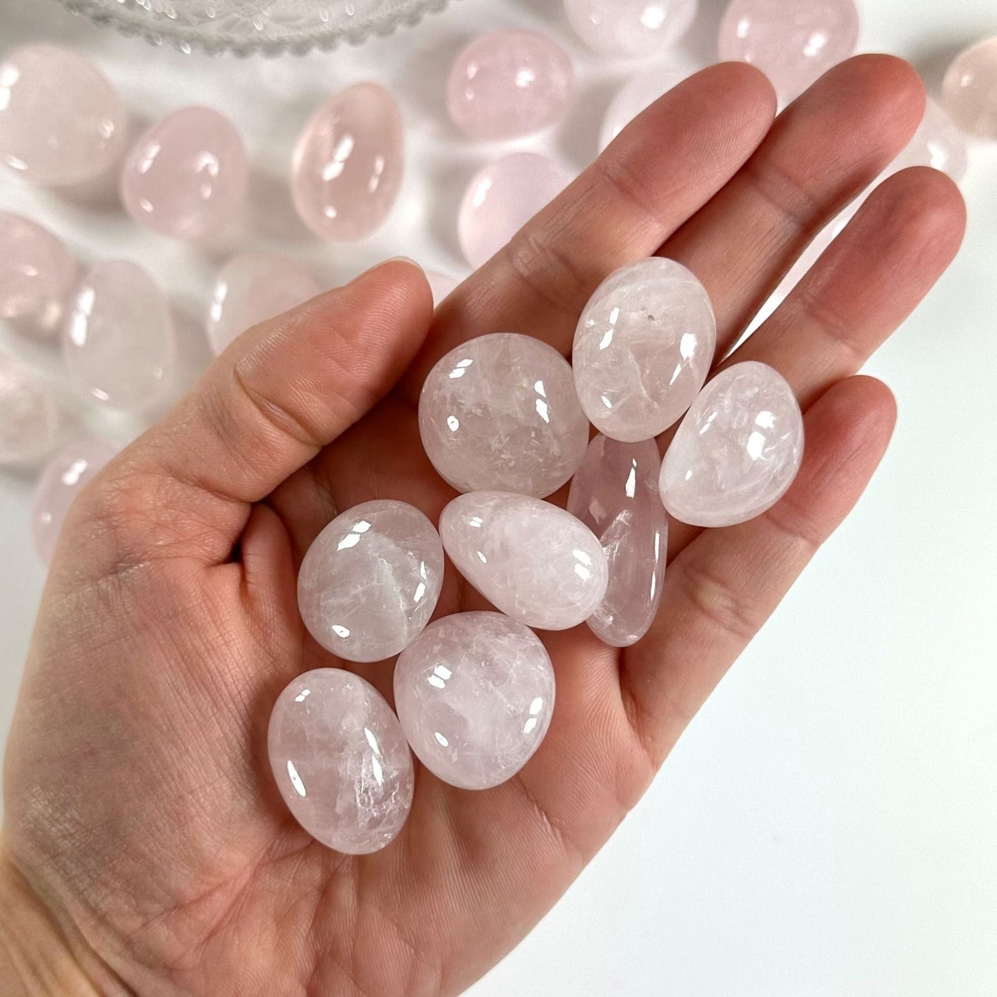 Hånd med flere rosenkvarts lommesten mod en baggrund af lignende sten.