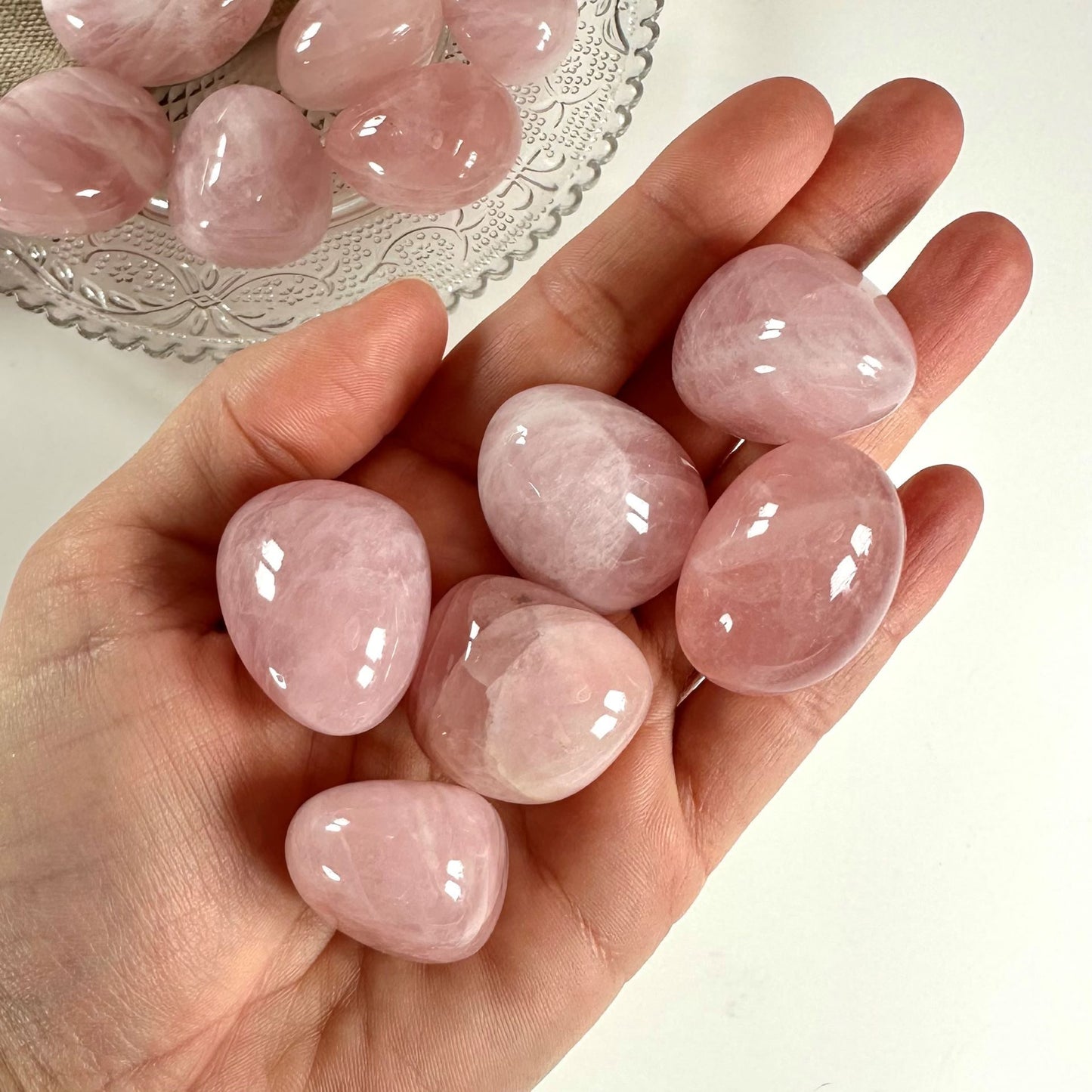 En hånd holder flere Rosenkvarts lommesten med bånd; flere sten på en tallerken i baggrunden.