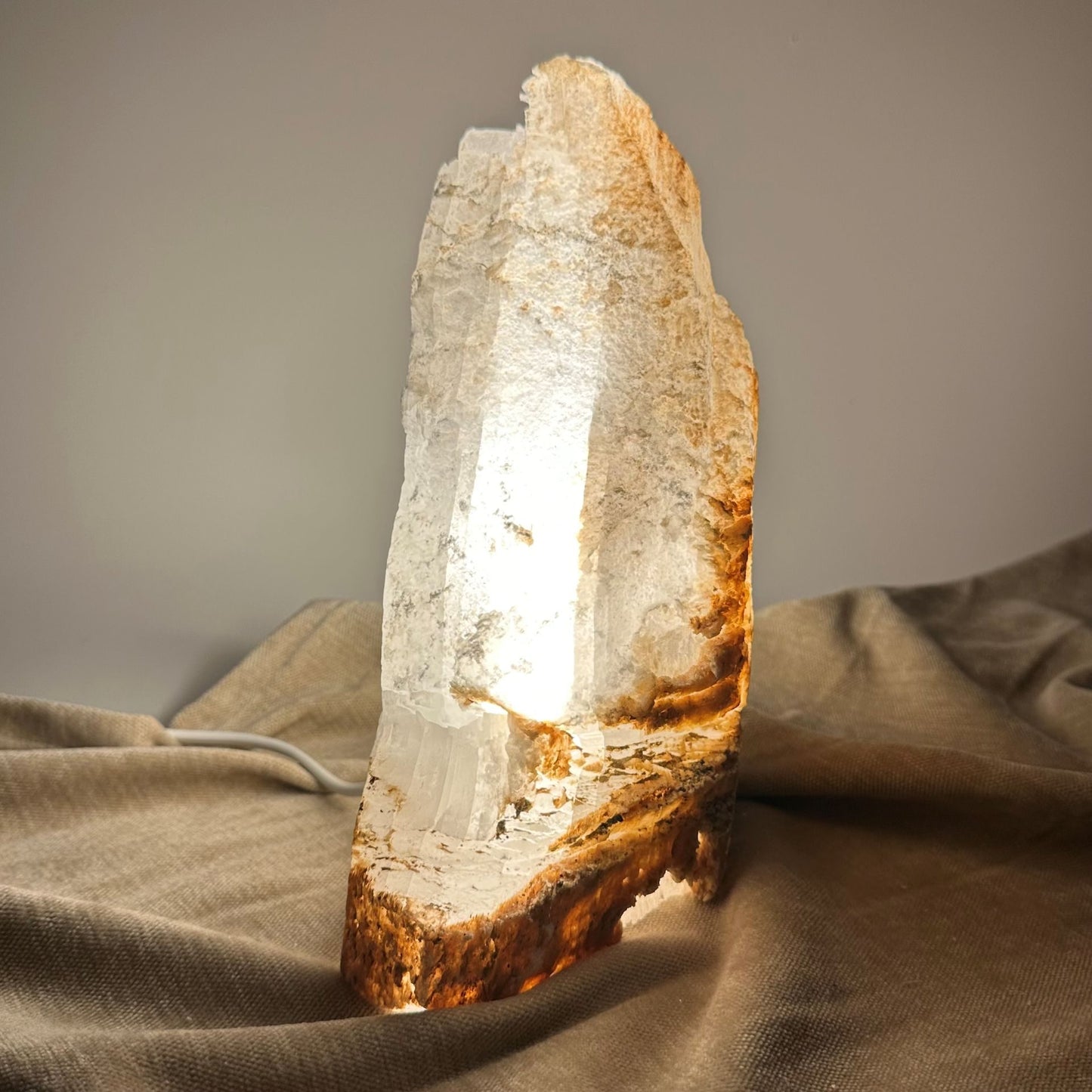 Mexicansk Selenit lampe nr 49, oplyst og placeret på tekstil, viser smukke naturlige striber og teksturer i varmt lys.
