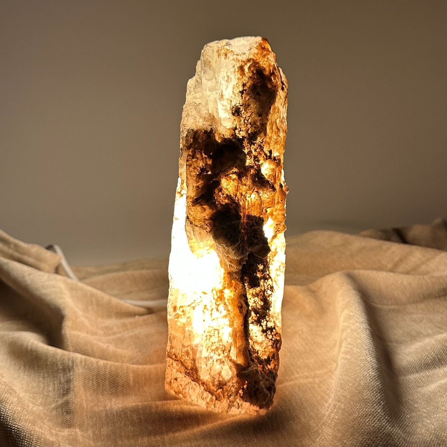 Mexicansk Selenit lampe nr 51 lyser op på en beige overflade, med sine naturlige, rå detaljer tydeligt synlige.