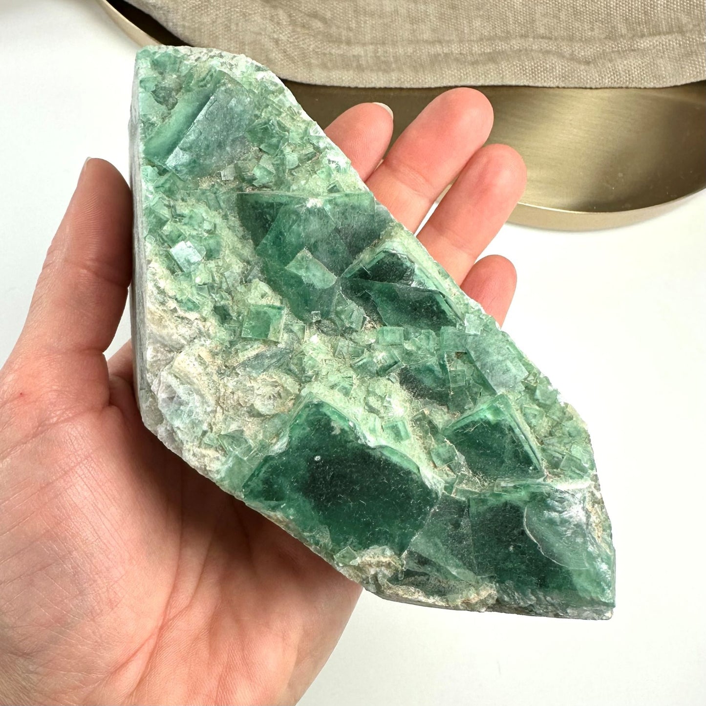 Hånd, der holder en stor grøn fluorit klynge med klare og uregelmæssige krystalstrukturer.