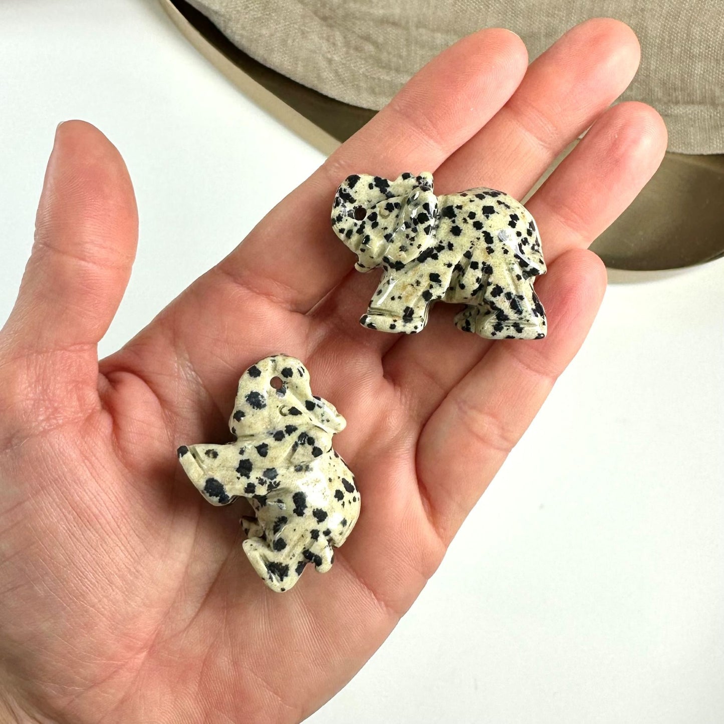 Hånden holder to små Dalmatiner elefantfigurer med sorte prikker på en lys baggrund.