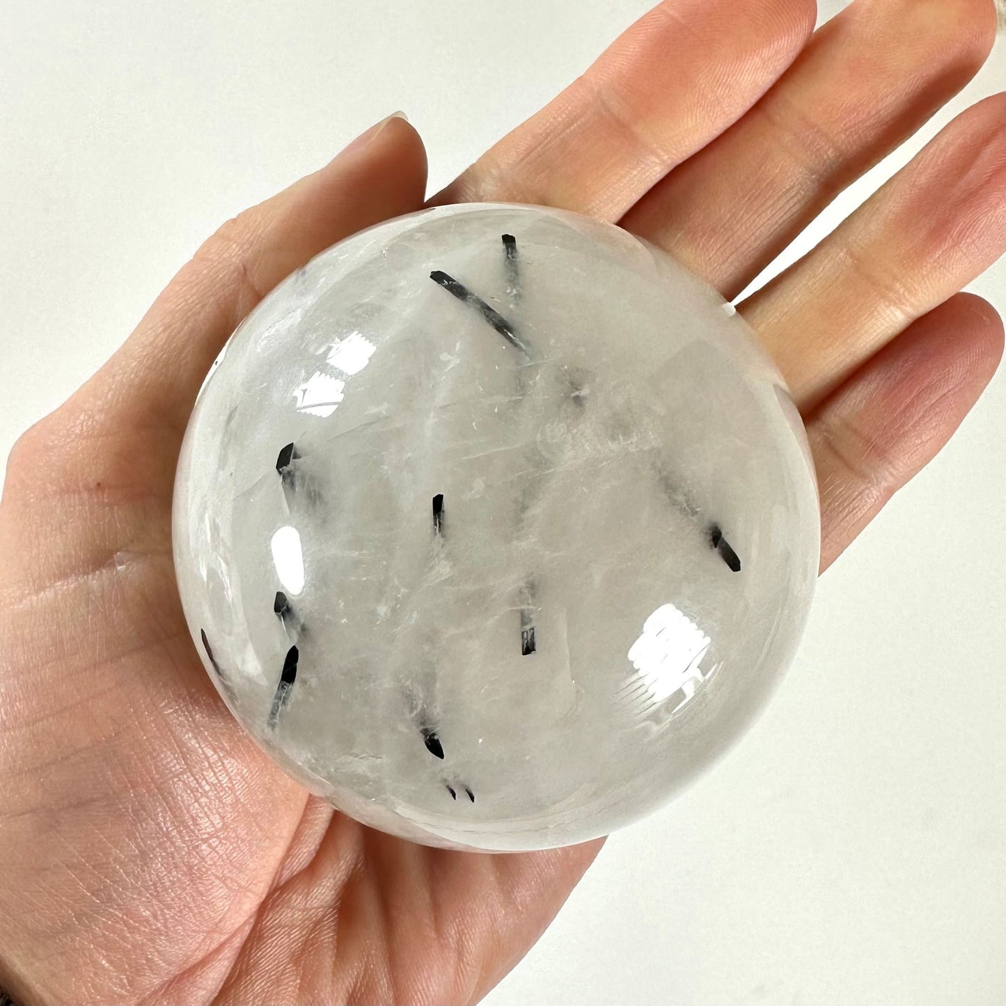 En hånd holder en turmalinkvarts kugle med sorte nåle inklusioner.