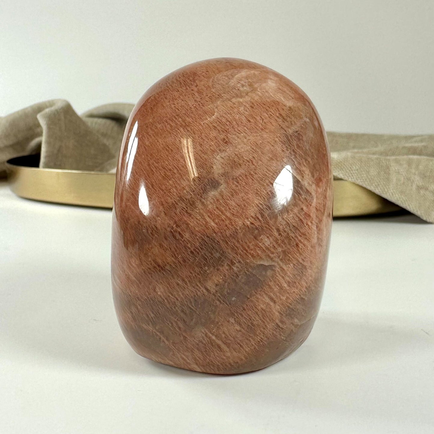 Fersken Månesten i fri form på bord, baggrund med beige stof og gyldent bakke.