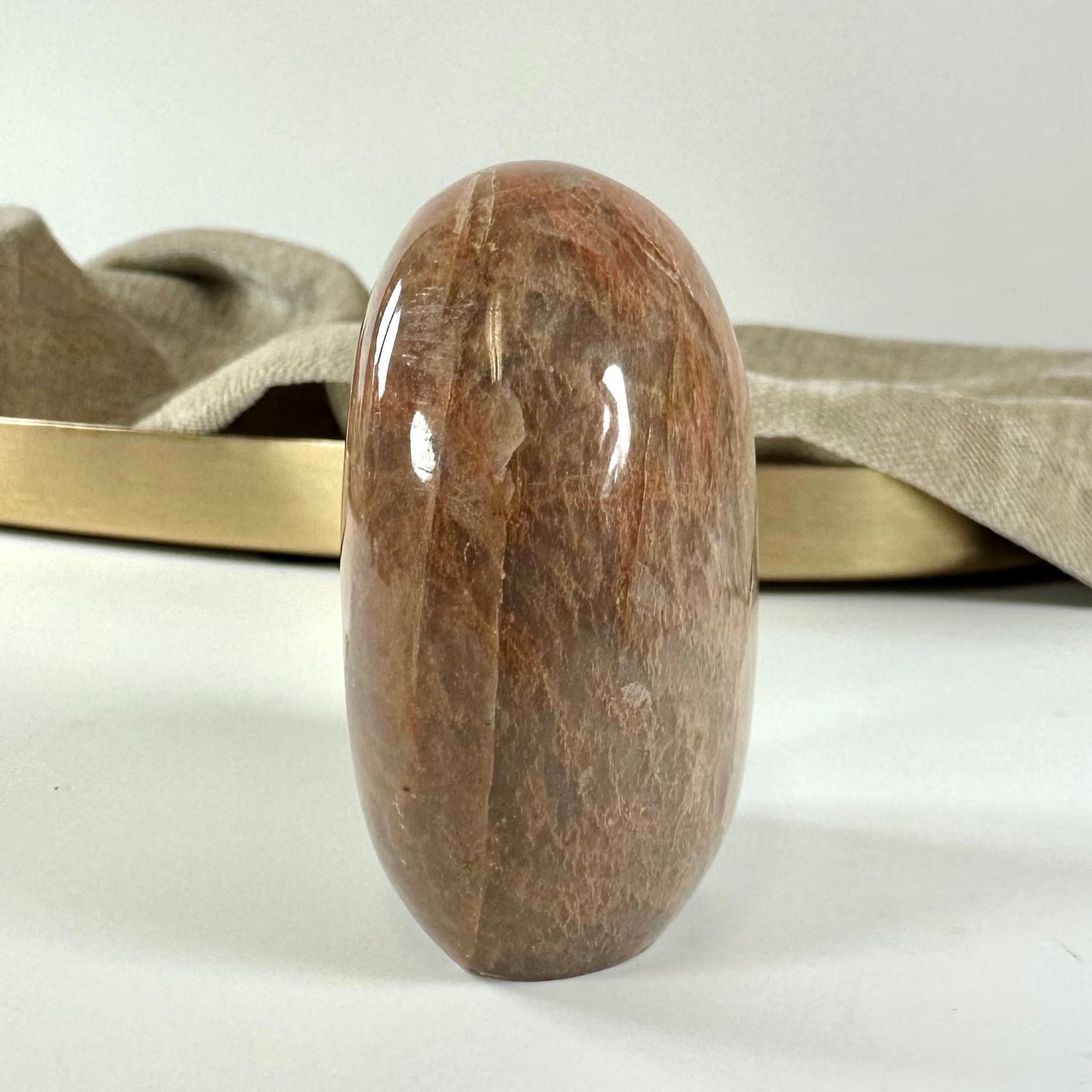 Fersken månesten i fri form står foran en beige stofbaggrund med en guldfarvet bakke.